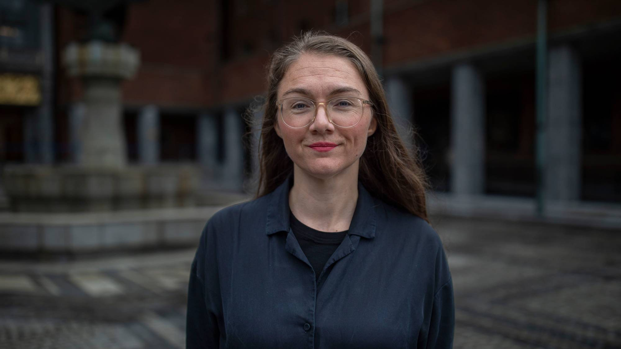 Portrett av en kvinne med briller foran Rådhusplassen i Oslo. (Bildebeskrivelsen er laget av en KI-tjeneste)