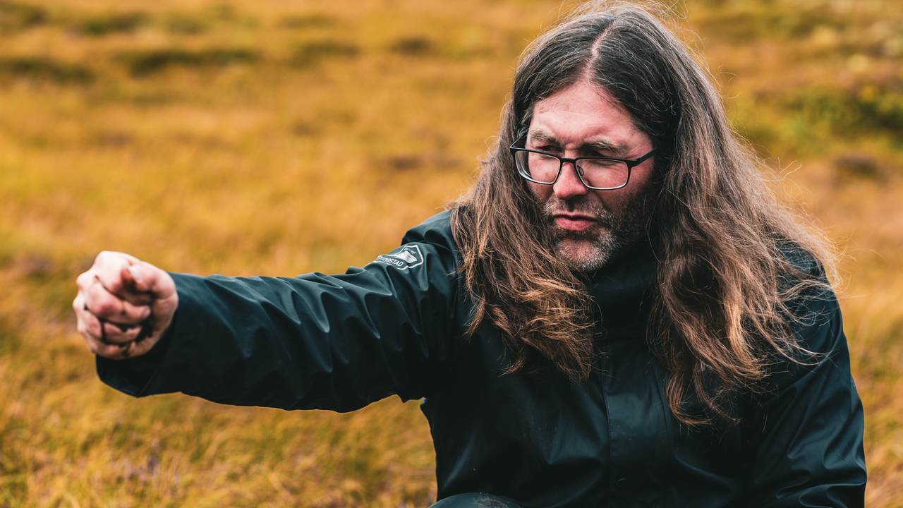 Nærbilde av Anders Lyngstad som klemmer ut vann av en neve med torv.