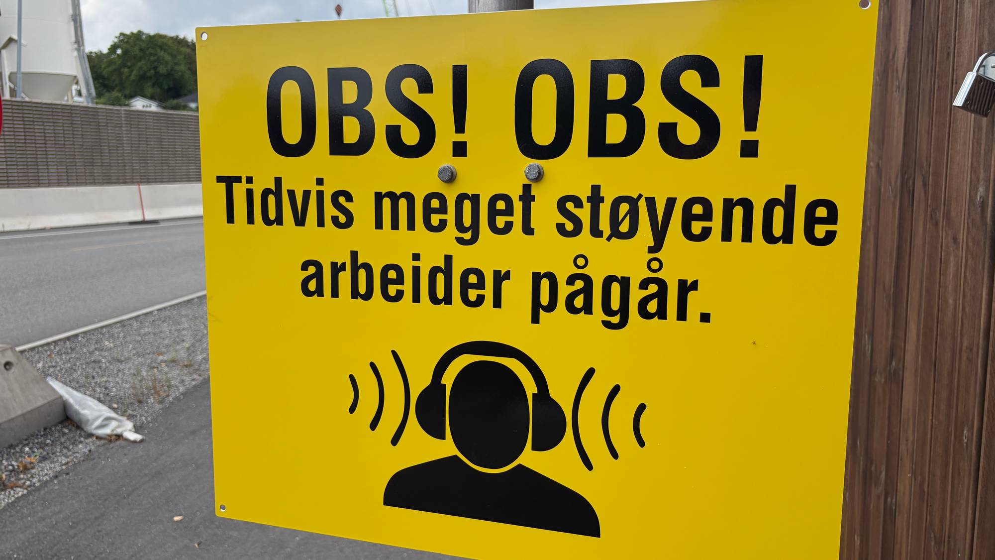 Gult skilt med advarsel om støyende arbeid ved en anleggsplass. (Bildebeskrivelsen er laget av en KI-tjeneste)