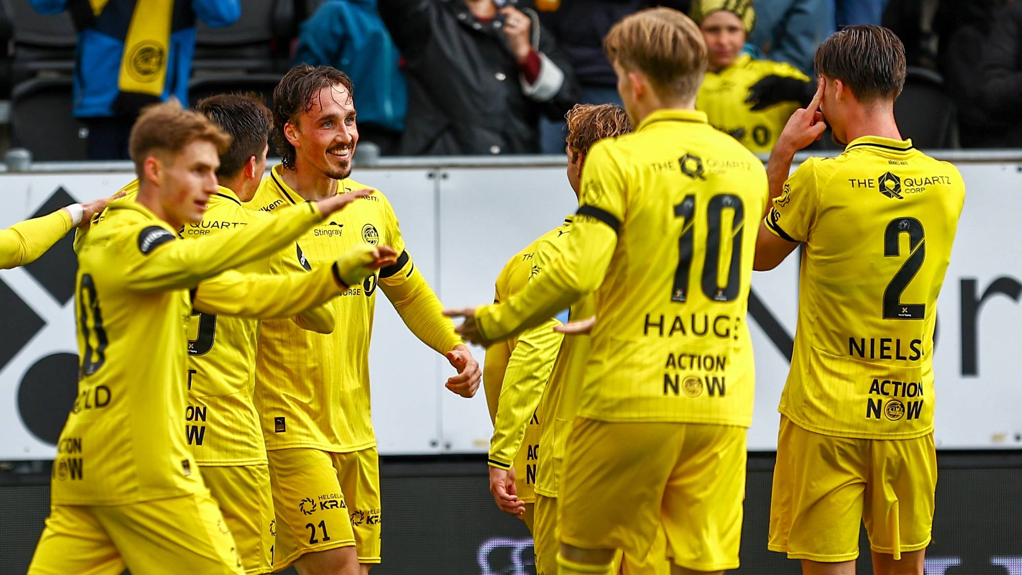 Fotballspillere i gule drakter jubler sammen på banen etter scoring. (Bildebeskrivelsen er laget av en KI-tjeneste)