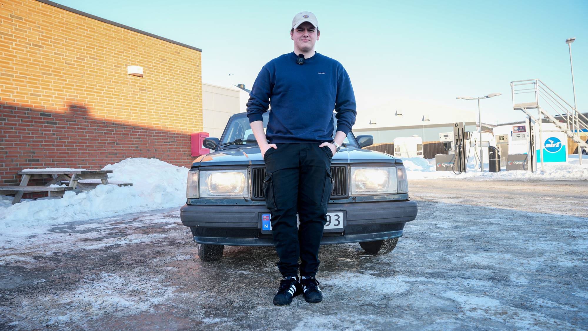 Ung mann, med mørkeblå genser og caps kjører Volvo 240