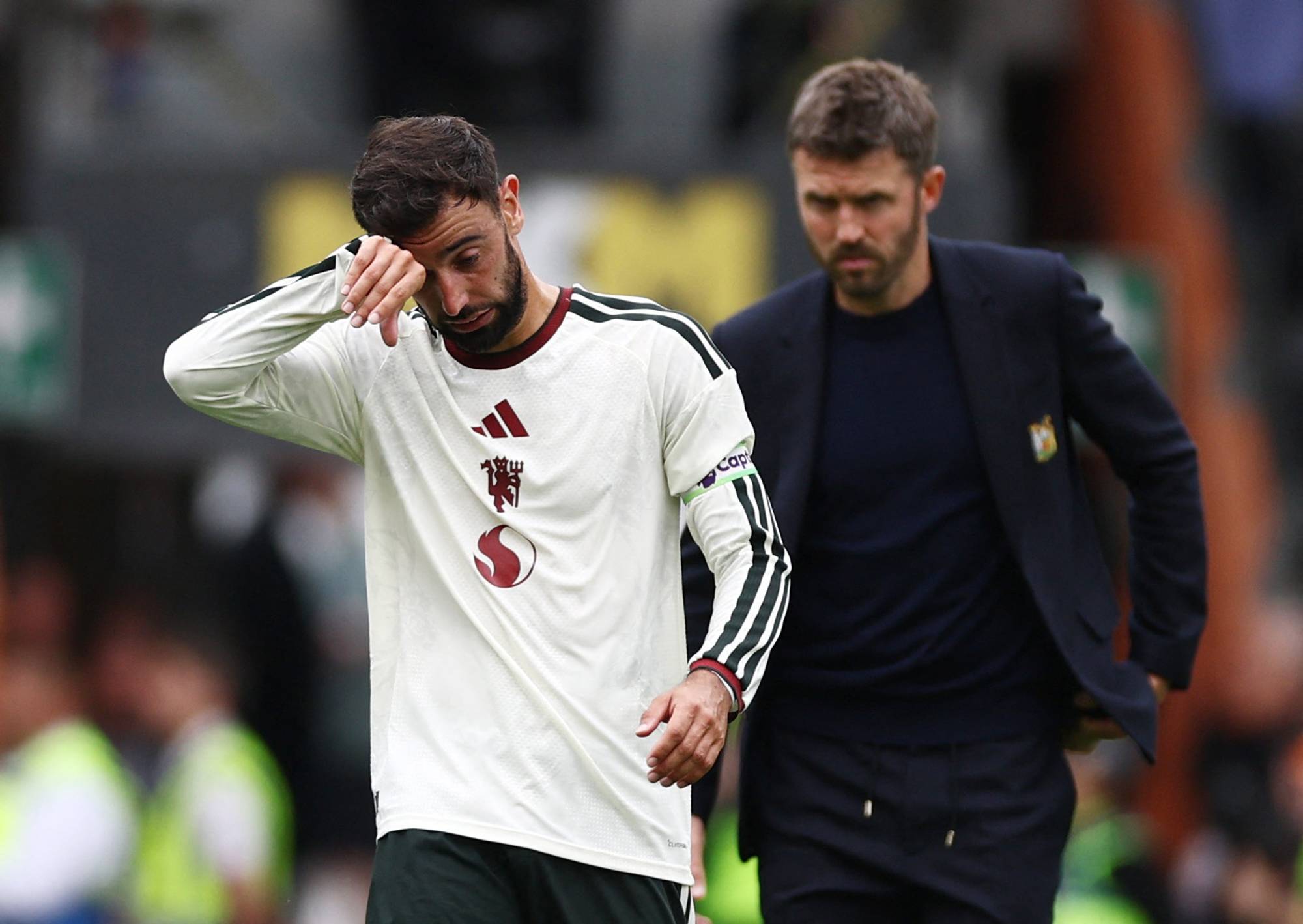 Bruno Fernandes tørker seg i ansiktet ved siden av trener Michael Carrick på en fotballbane. (Bildebeskrivelsen er laget av en KI-tjeneste)