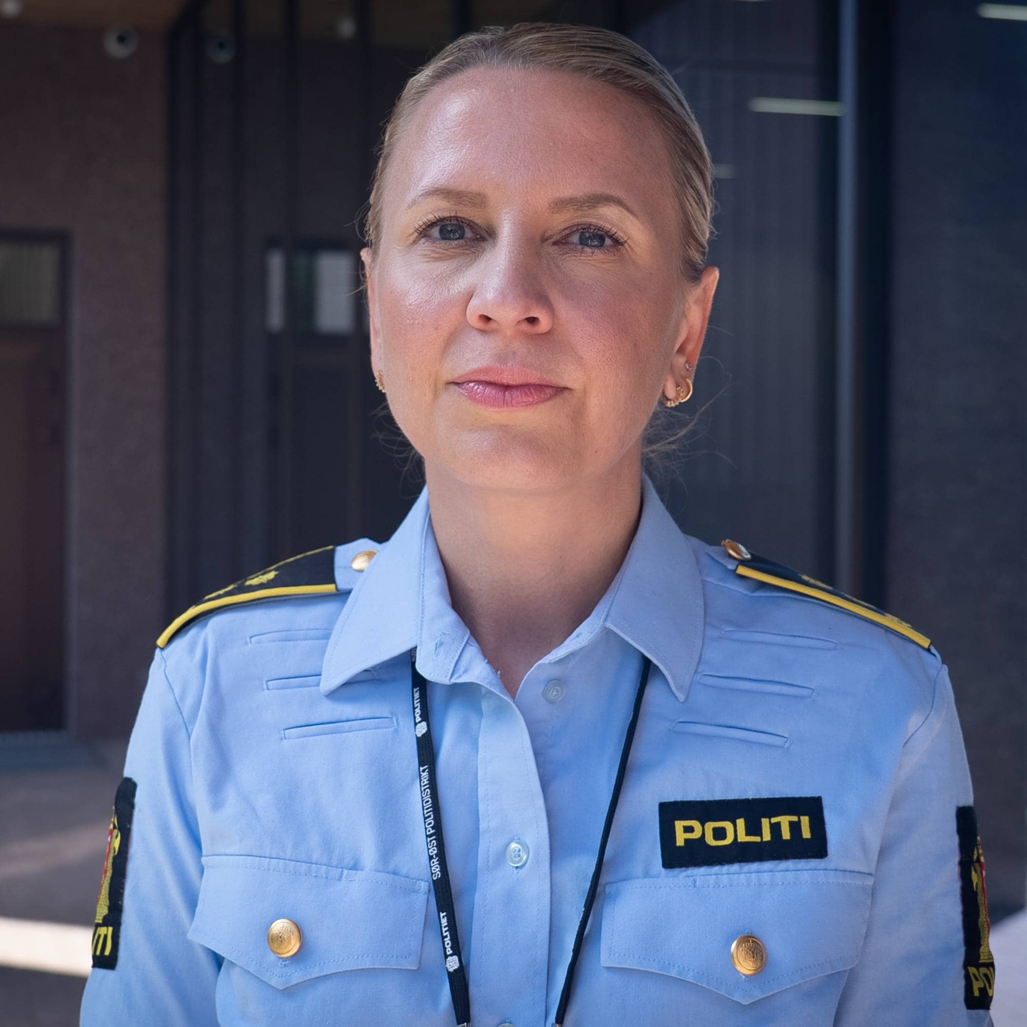Portrett av en kvinnelig politibetjent i uniform, stående foran en bygning.