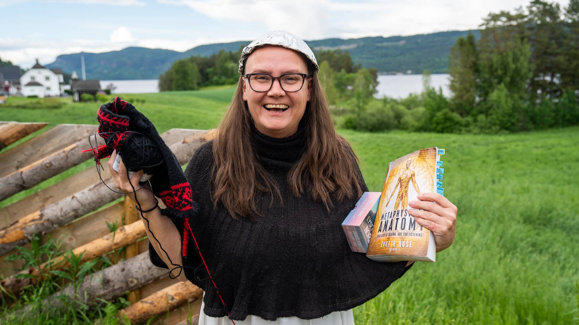 Lena Nordstrøm holder strikketøy, tarotkort og en bok, samtidig som hun har tinnfolie på hodet og smiler stort
