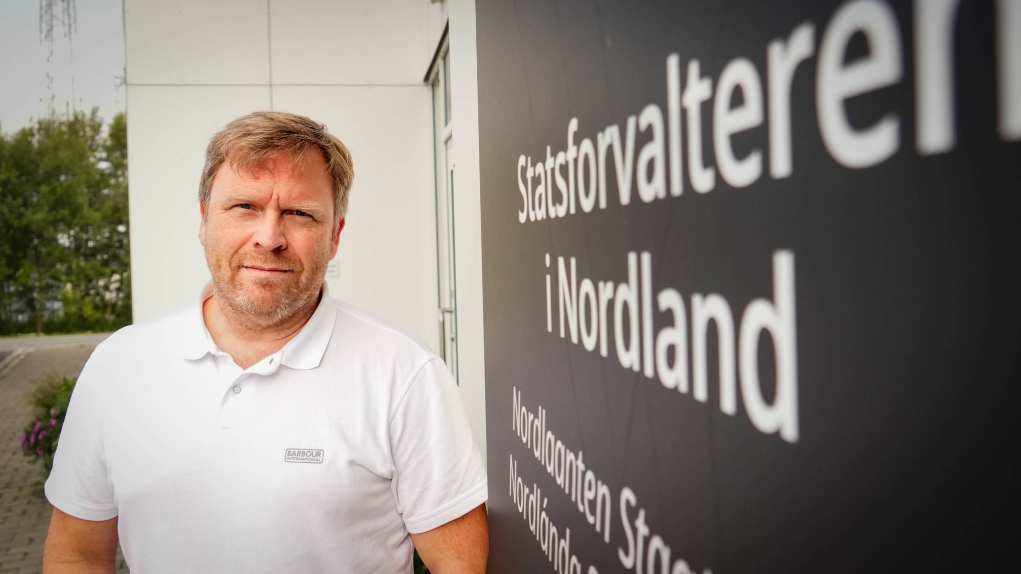 Mann med hvit piquetskjorte som ser i kameraet.