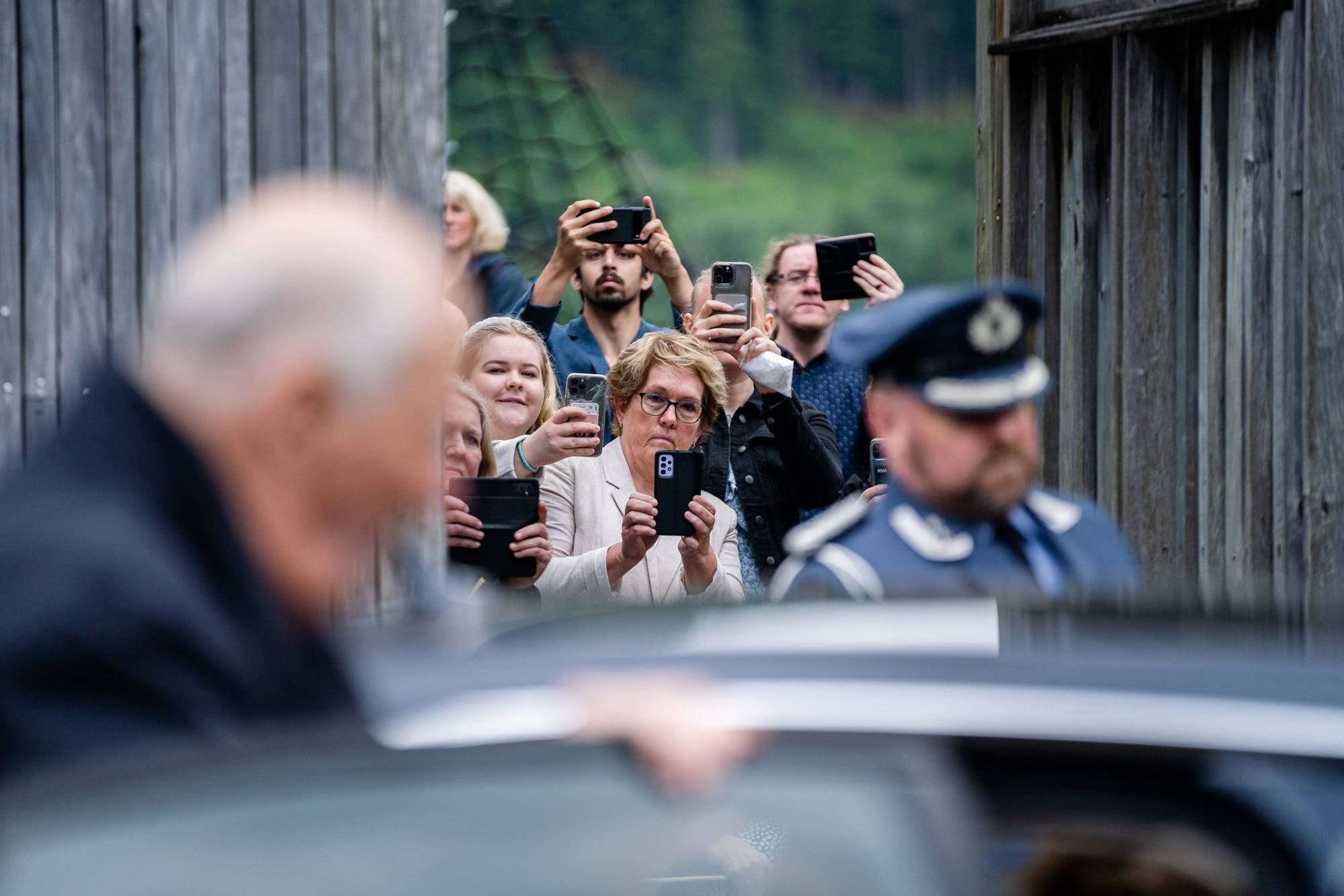 En gruppe mennesker tar bilder av kong Harald med mobiltelefonen sine, mens han går inn i den ventende bilen under fylkesreisen i Agder i 2024