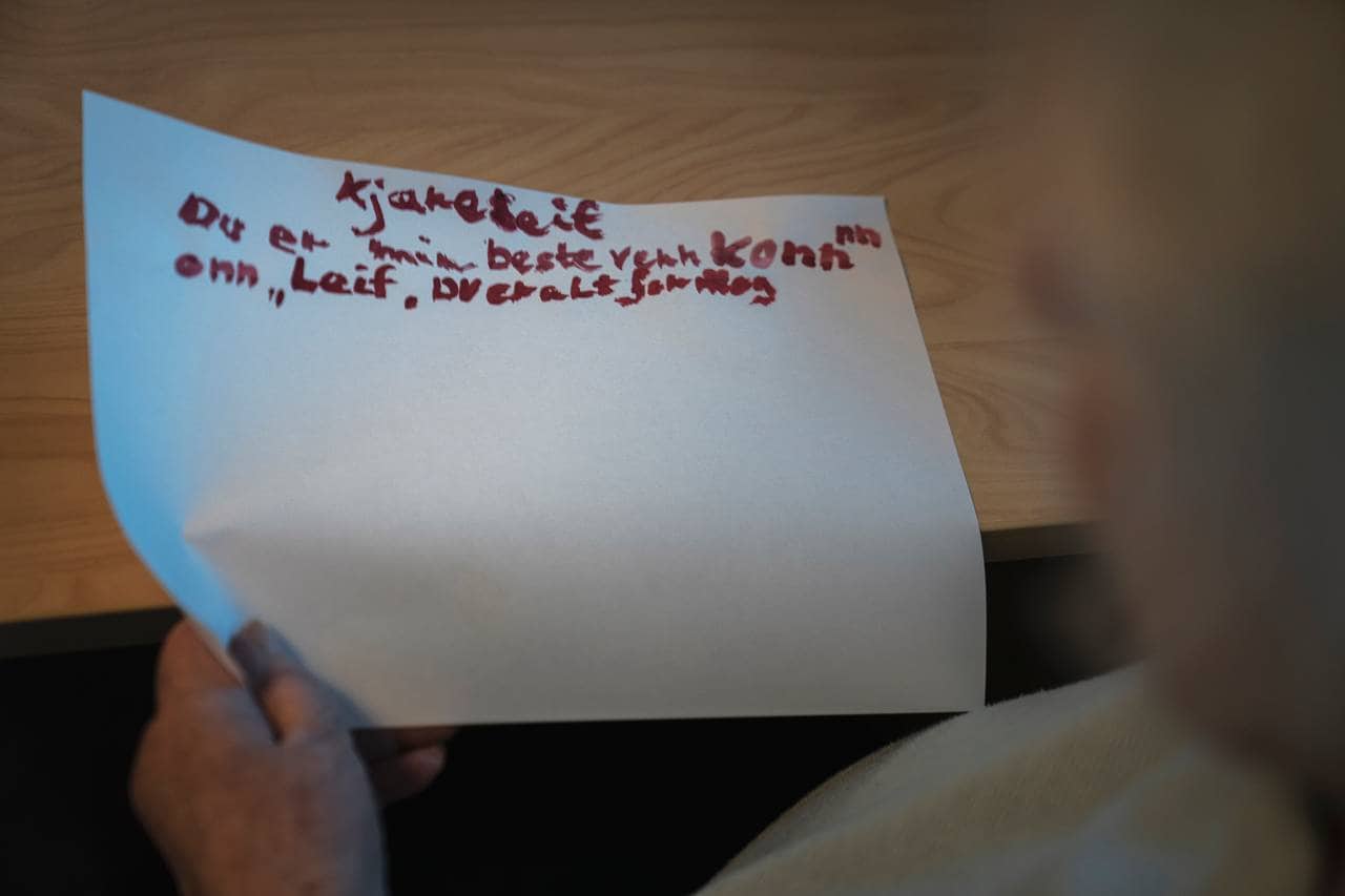 Anne Marie holder i et ark med brevet hun har skrevet til Leif. Der står det "Kjære Leif, du er min beste venn komm onn, Leif, du er alt for meg"