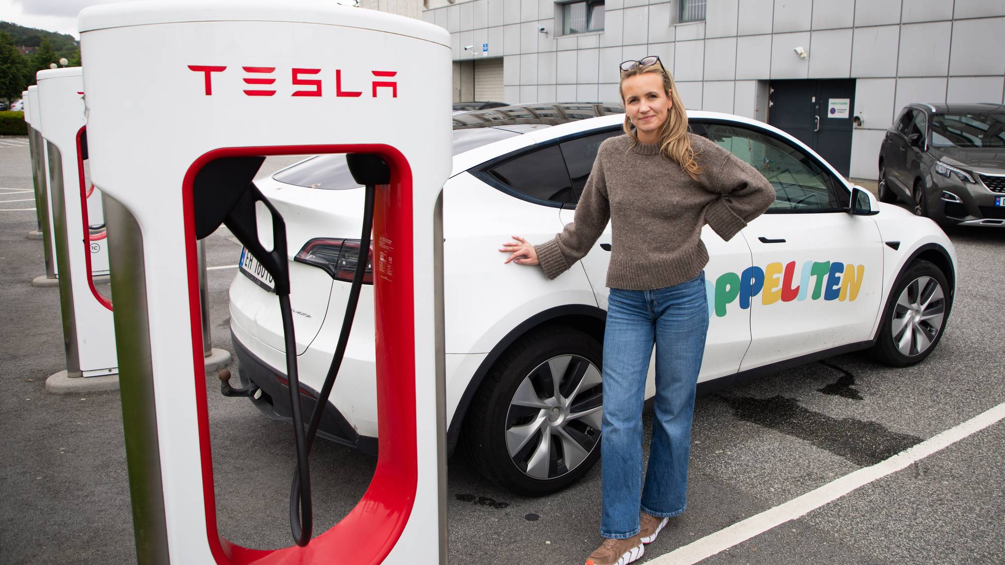 Kvinne står foran en hvit Tesla.