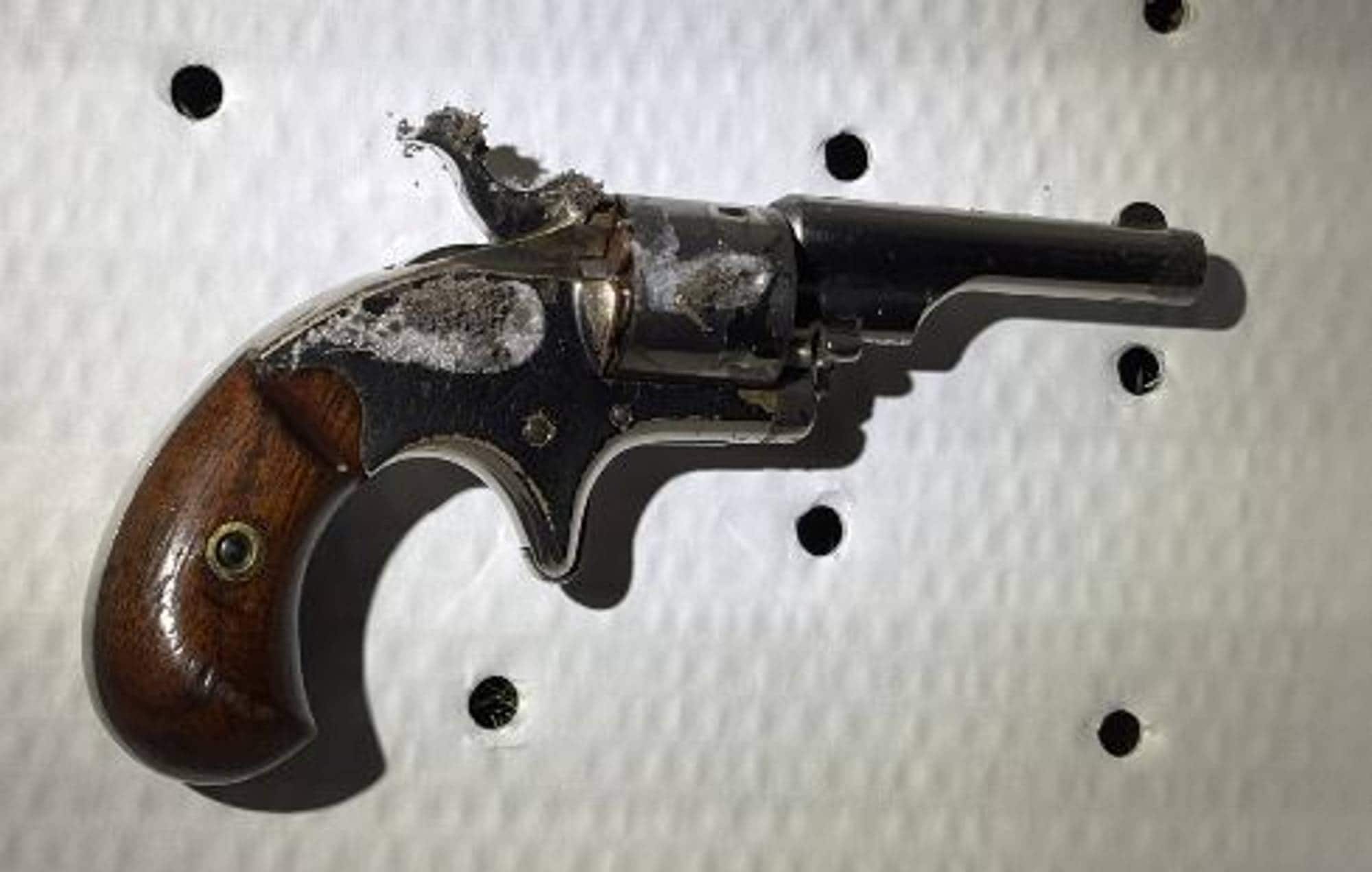En eldre revolver med treverk i skjeftet ligger på en hvit, perforert plate.