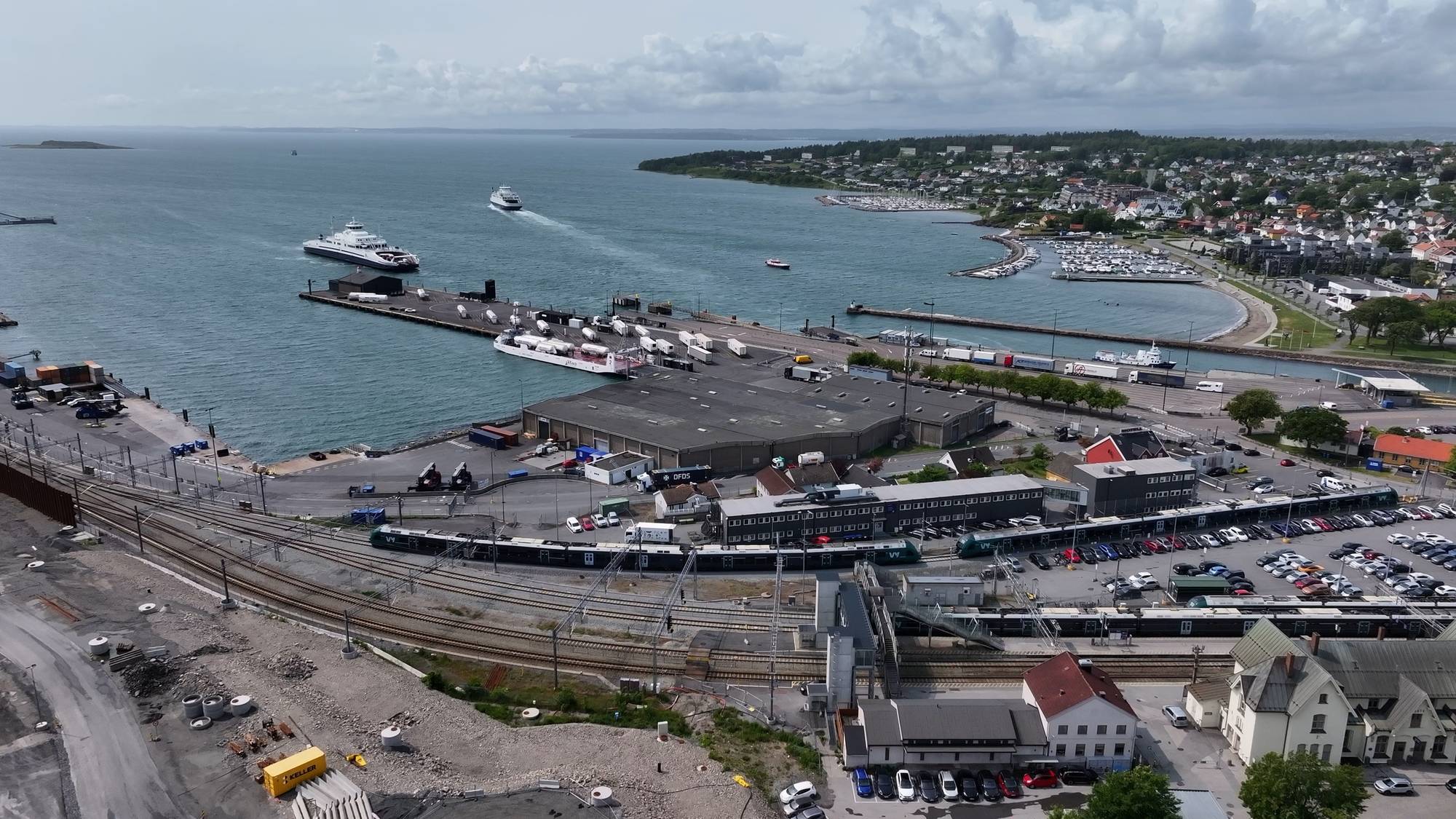 Flyfoto av fergekai og togstasjon i Moss med skip, kjøretøy og bebyggelse. (Bildebeskrivelsen er laget av en KI-tjeneste)