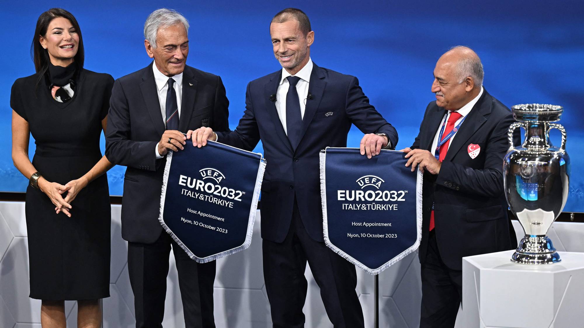 Representanter fra Italia og Tyrkia holder bannere for fotball-EM i 2032 sammen med Aleksander Ceferin. (Bildebeskrivelsen er laget av en KI-tjeneste)
