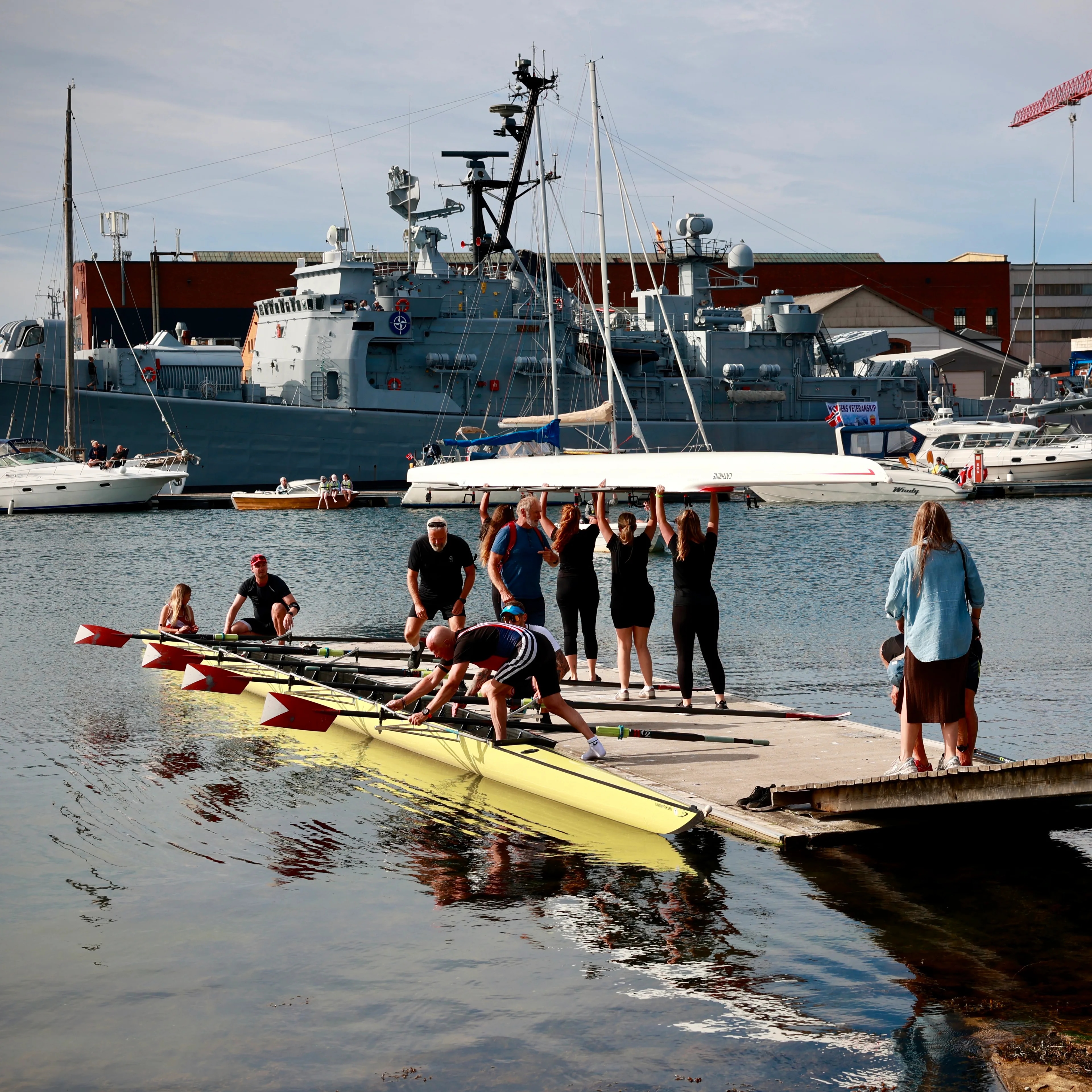 Roere bærer en båt på en flytebrygge med et marinefartøy i bakgrunnen.