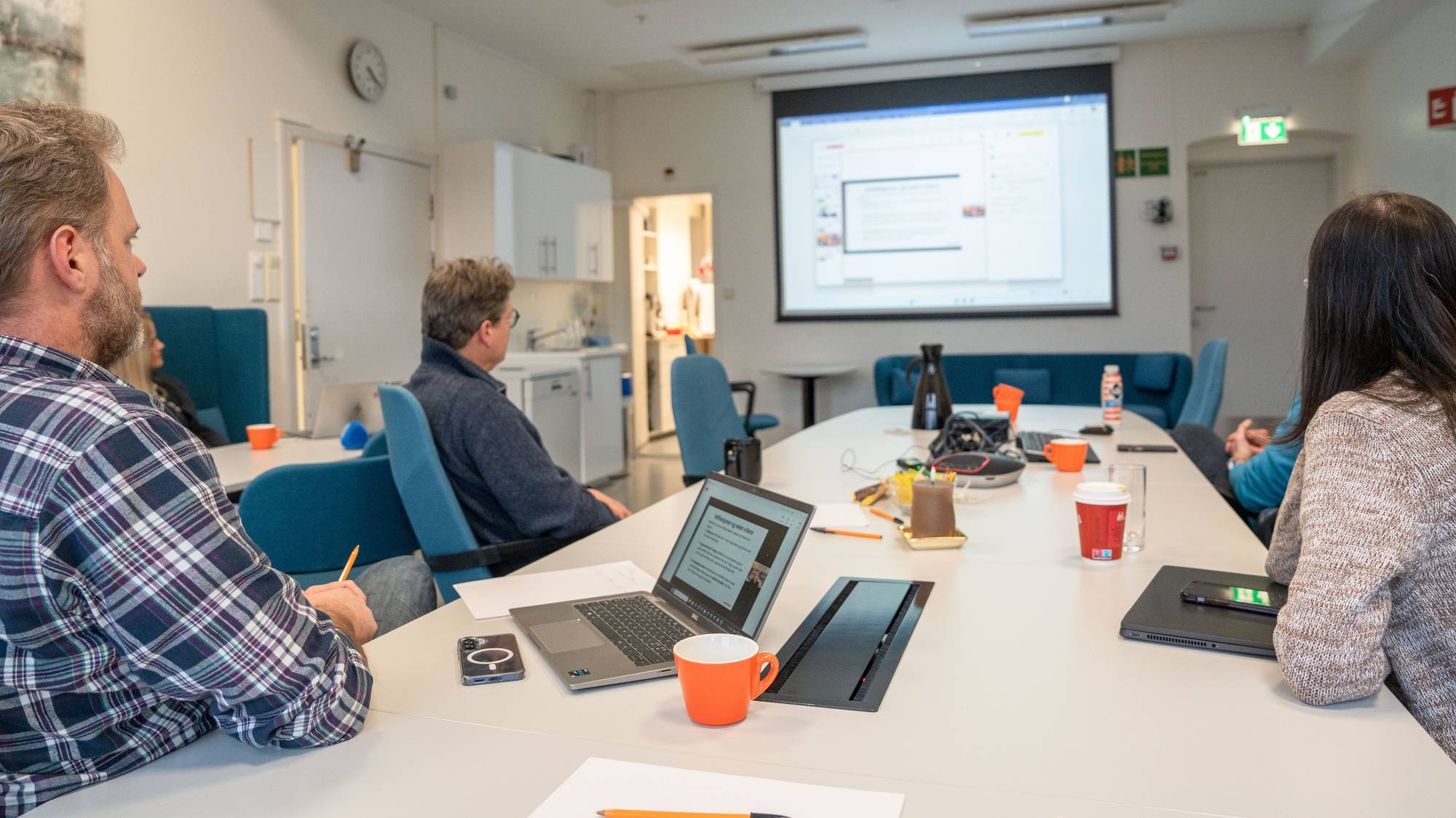 Mennesker rundt et bord ser på en presentasjon.