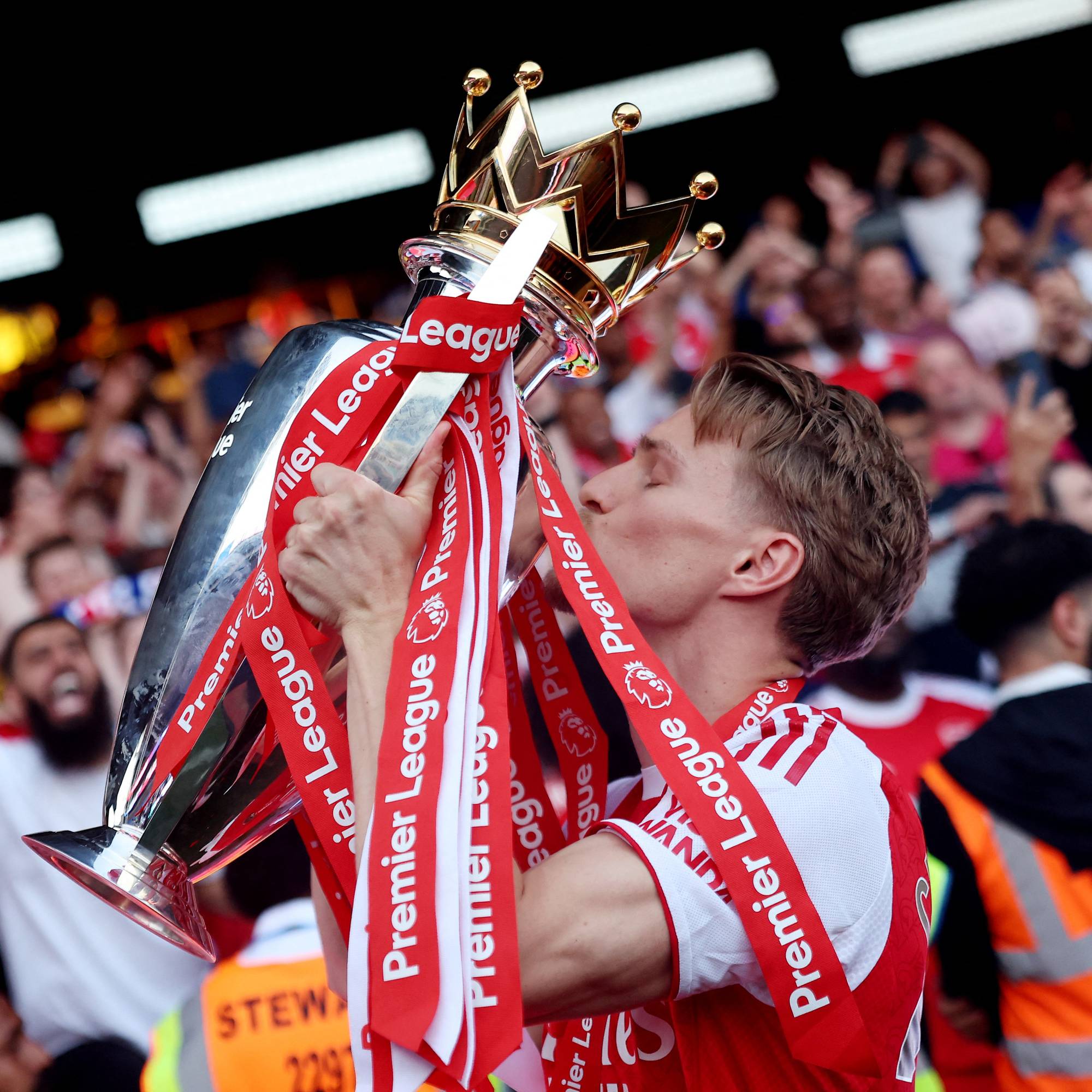 Martin Ødegaard kysser Premier League-trofeet foran jublende supportere. (Bildebeskrivelsen er laget av en KI-tjeneste)