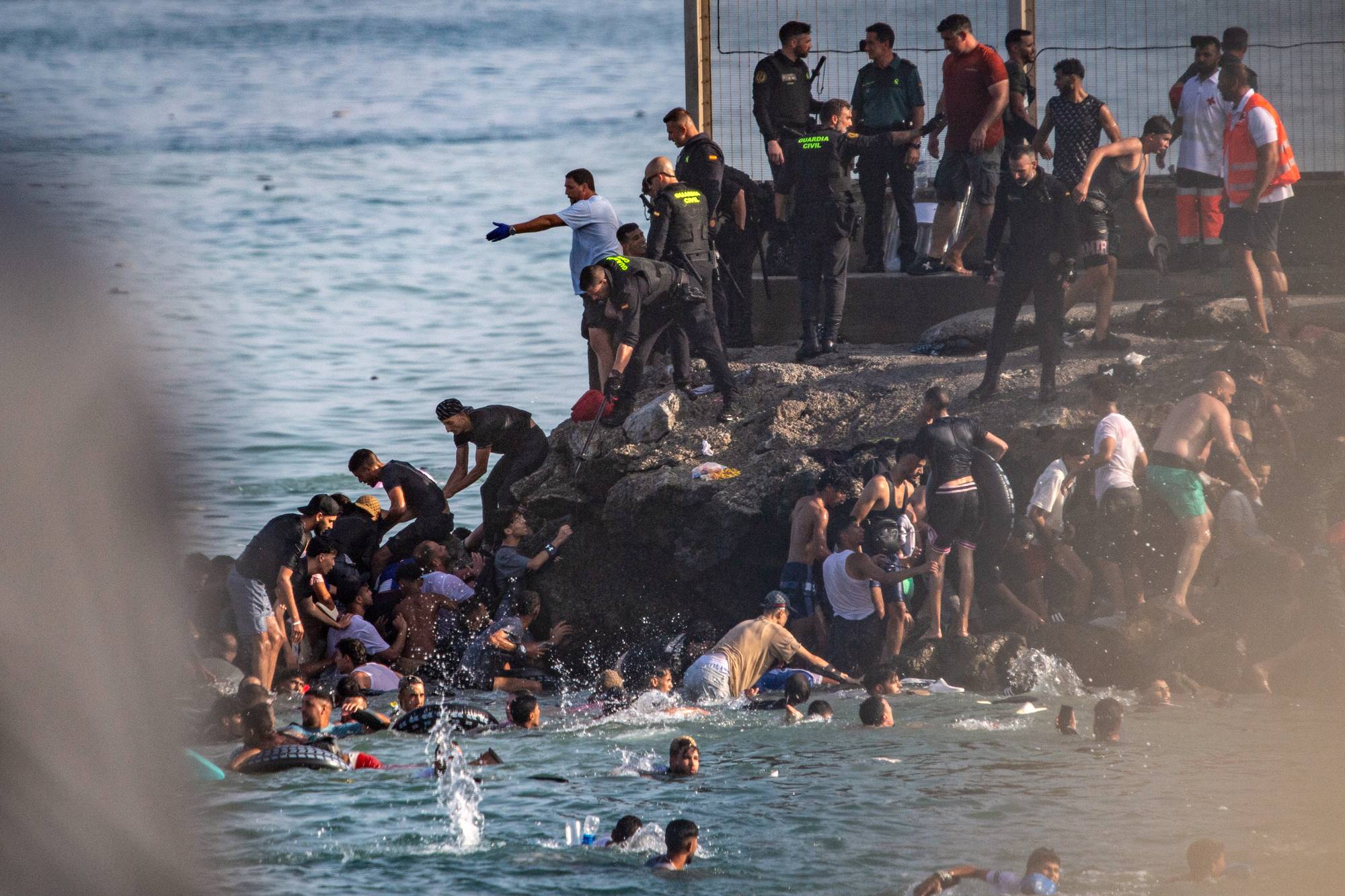 Migranter går i land fra små båter ved en kyst, mens spansk politi bistår på land. (Bildebeskrivelsen er laget av en KI-tjeneste)