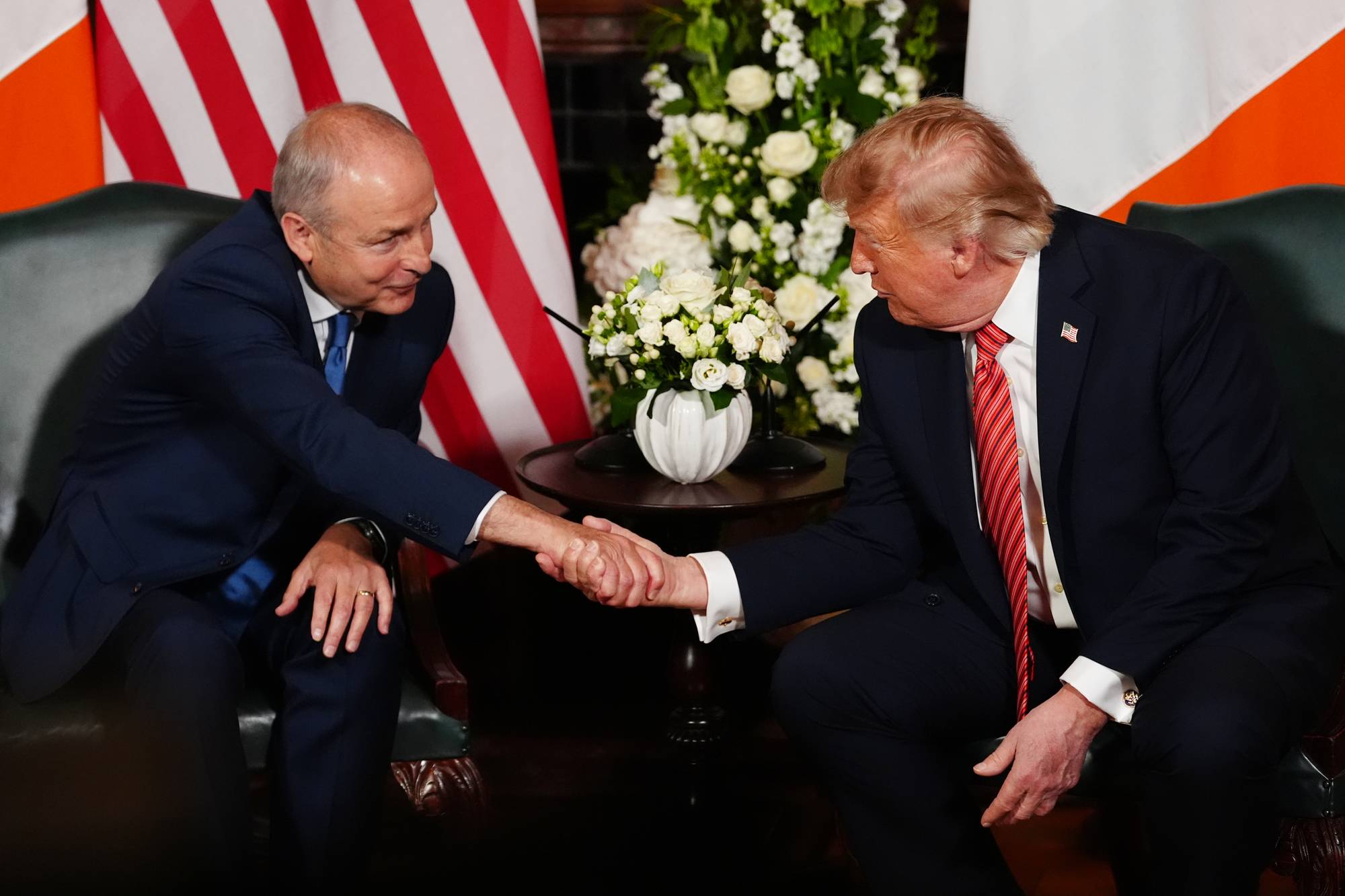 Micheál Martin og Donald Trump håndhilser mens de sitter i stoler foran amerikanske flagg. (Bildebeskrivelsen er laget av en KI-tjeneste)