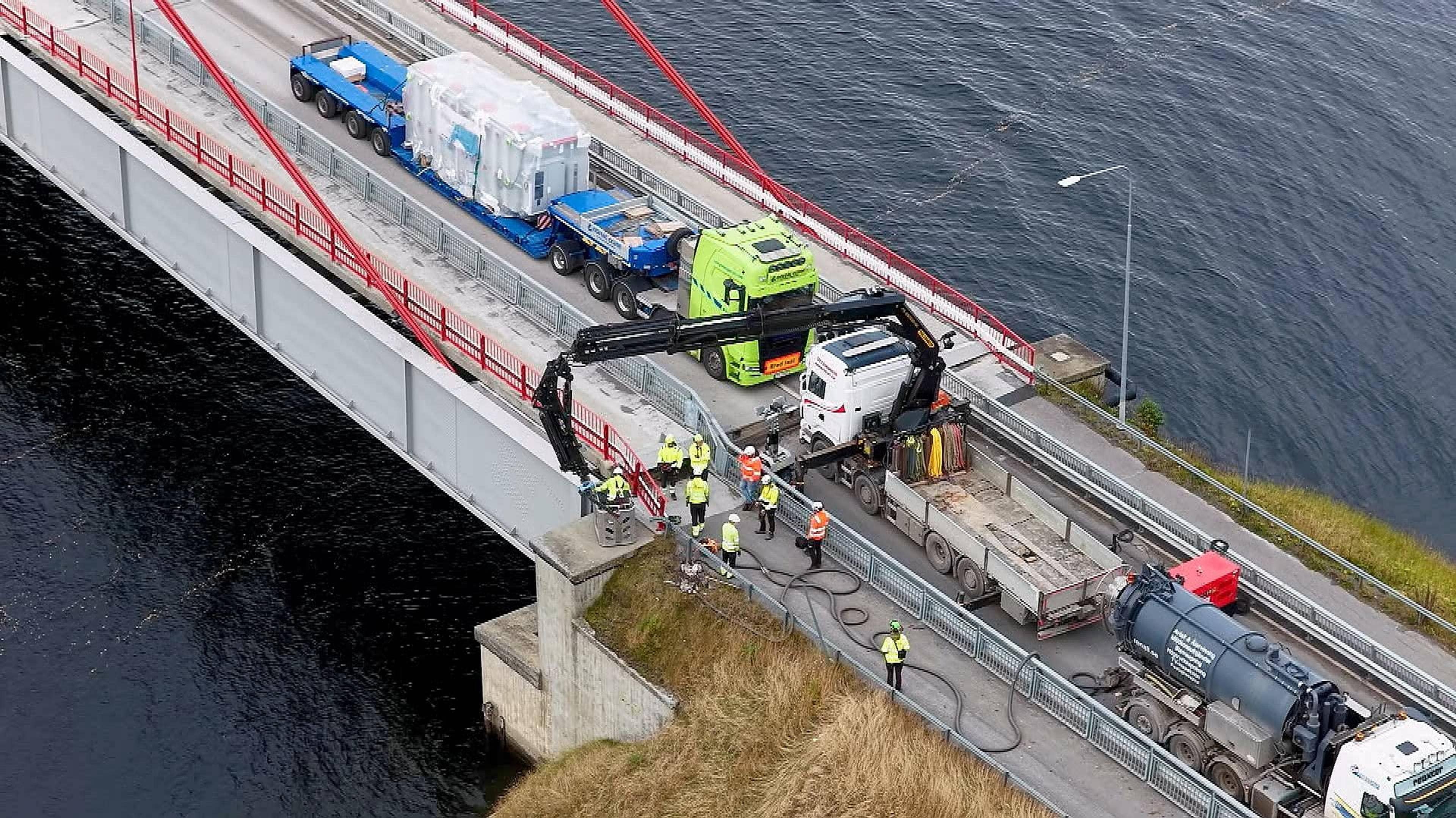 Arbeidere utfører vedlikeholdsarbeid på en hengebro med tunge kjøretøy og maskiner til stede. (Bildebeskrivelsen er laget av en KI-tjeneste)