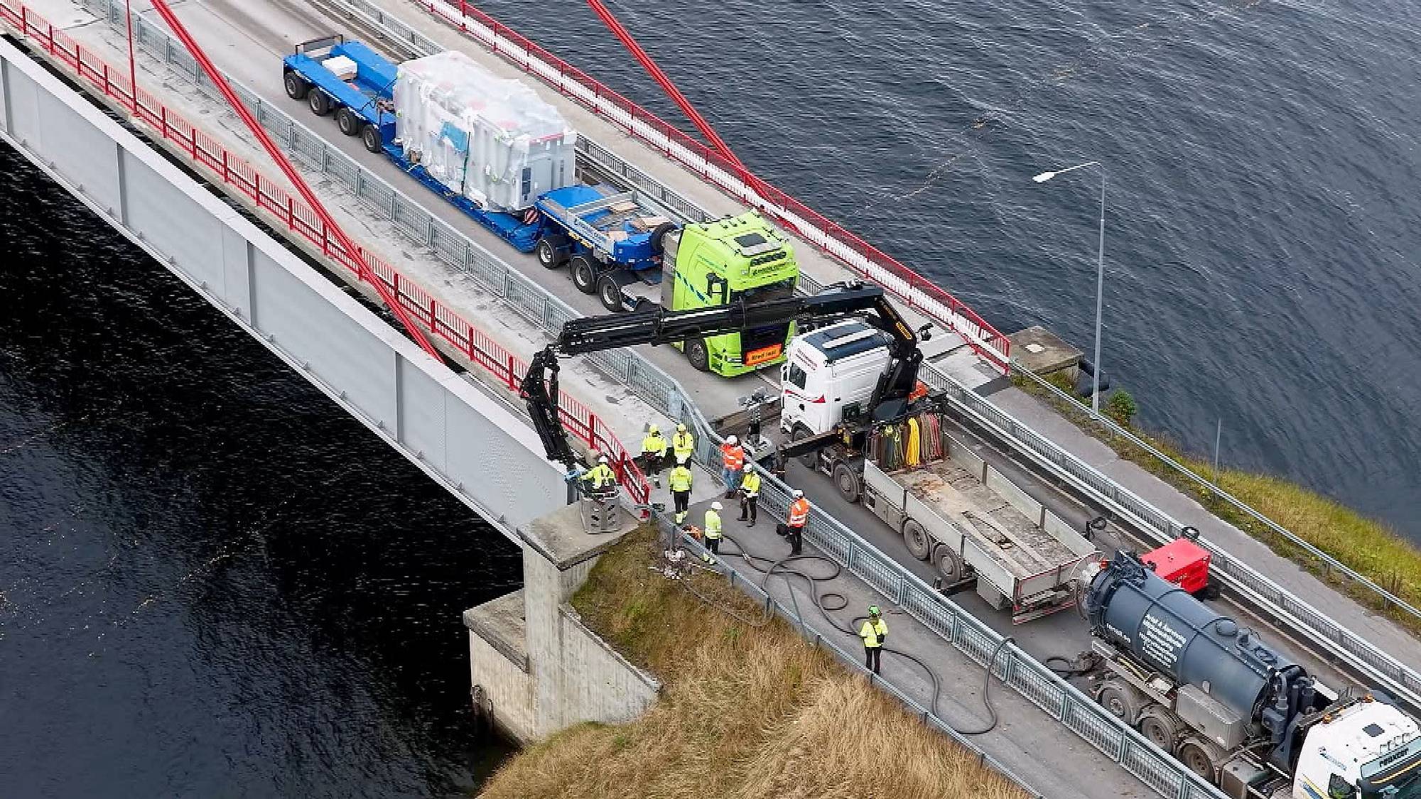 Arbeidere utfører vedlikeholdsarbeid på en hengebro med tunge kjøretøy og maskiner til stede. (Bildebeskrivelsen er laget av en KI-tjeneste)