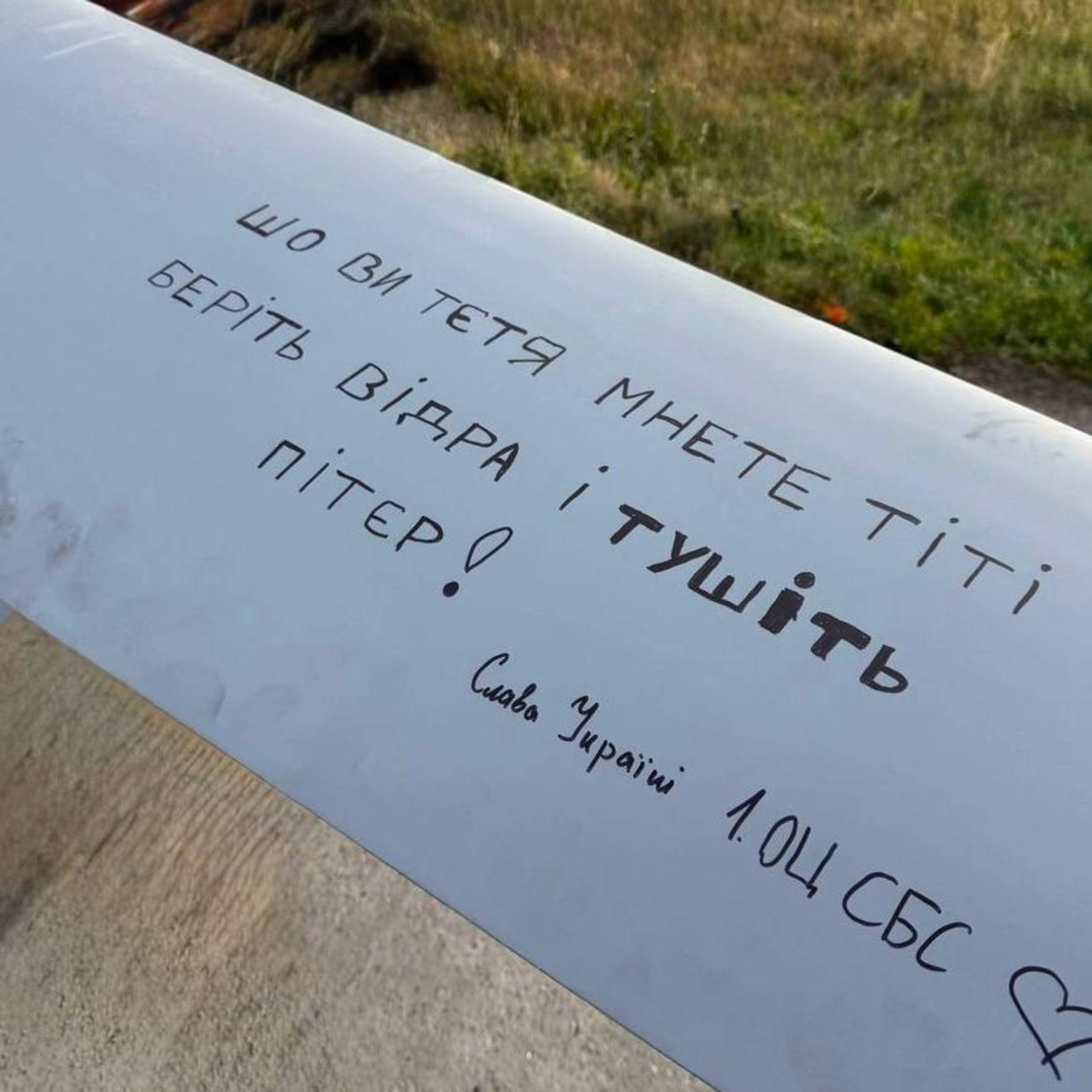 Et bilde av en drone med ukrainsk tekst.Teksten lyder "sho vy tetya mnetete titi berit vidra i tushit Piter!".Under er det skrevet "Slava Ukraini 1.Och SBS".Bildet viser en drone i en eng, med tekst skrevet på en av vingene. (Bildebeskrivelsen er laget av en KI-tjeneste)