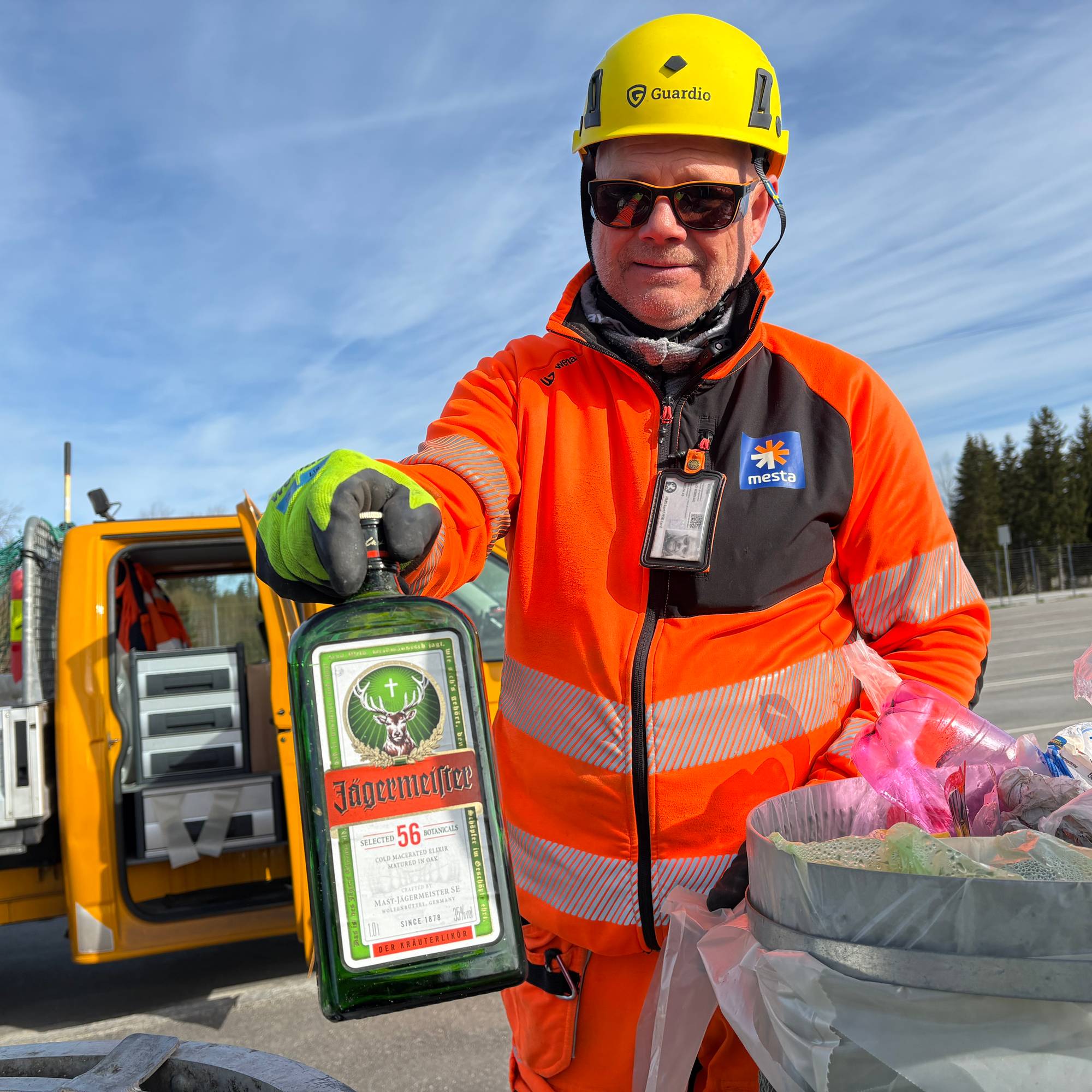 Tomas Nilsen fra Mesta i oransje jakke, solbriller og gul hjelm viser fram en tom flaske med Jägermeister han har tatt opp fra en søppeldunk, i bakgrunenn en liten lastebil. , I 