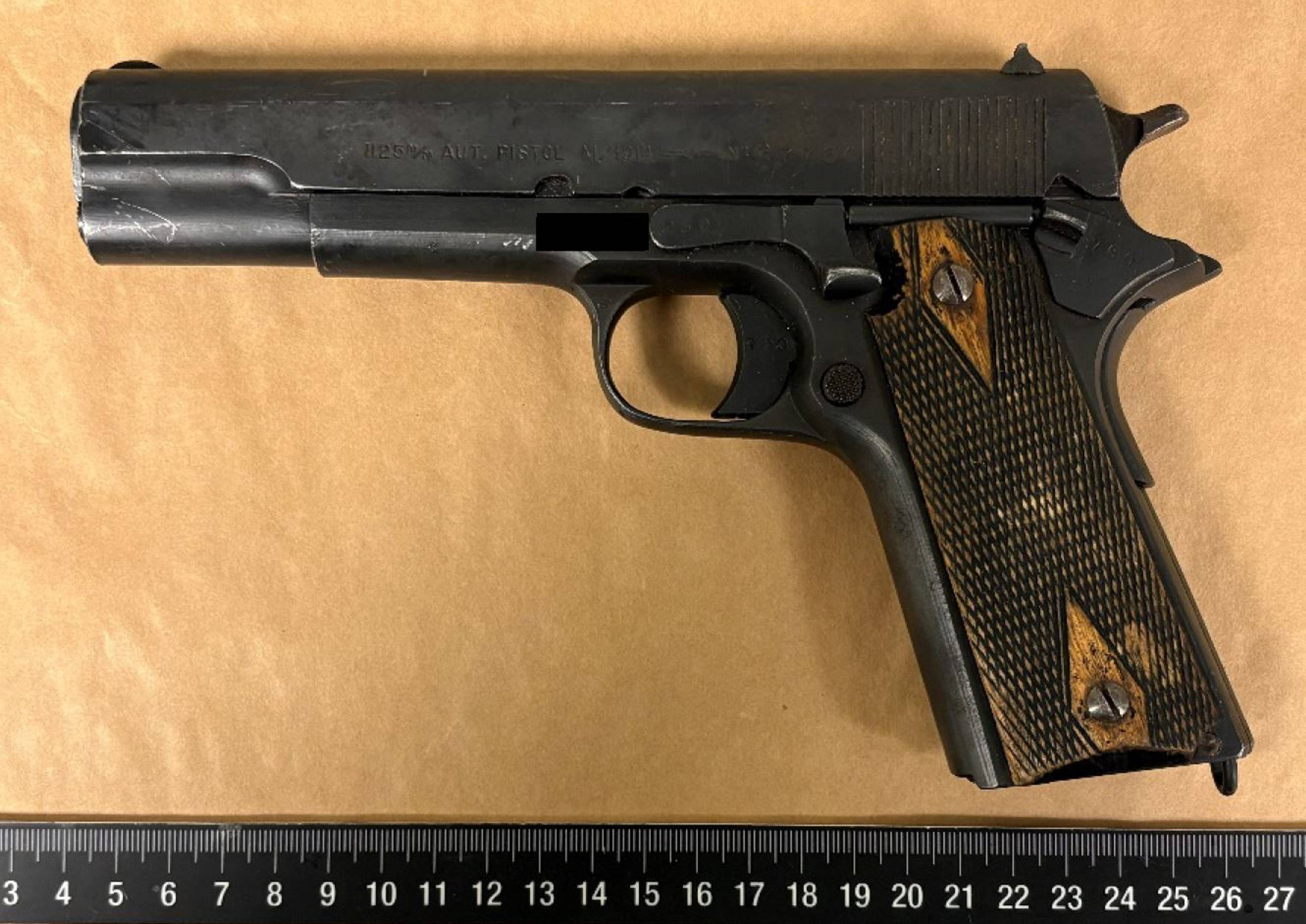 Et pistol ligger på en brun bakgrunn. En linjal er plassert nederst i bildet.