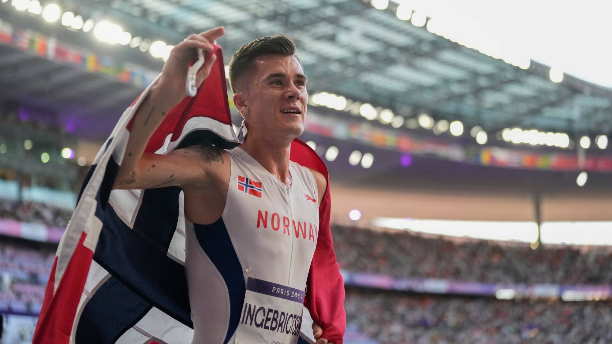 Jakob Ingebrigtsen feirer med norsk flagg på stadion under OL i Paris 2024. (Bildebeskrivelsen er laget av en KI-tjeneste)