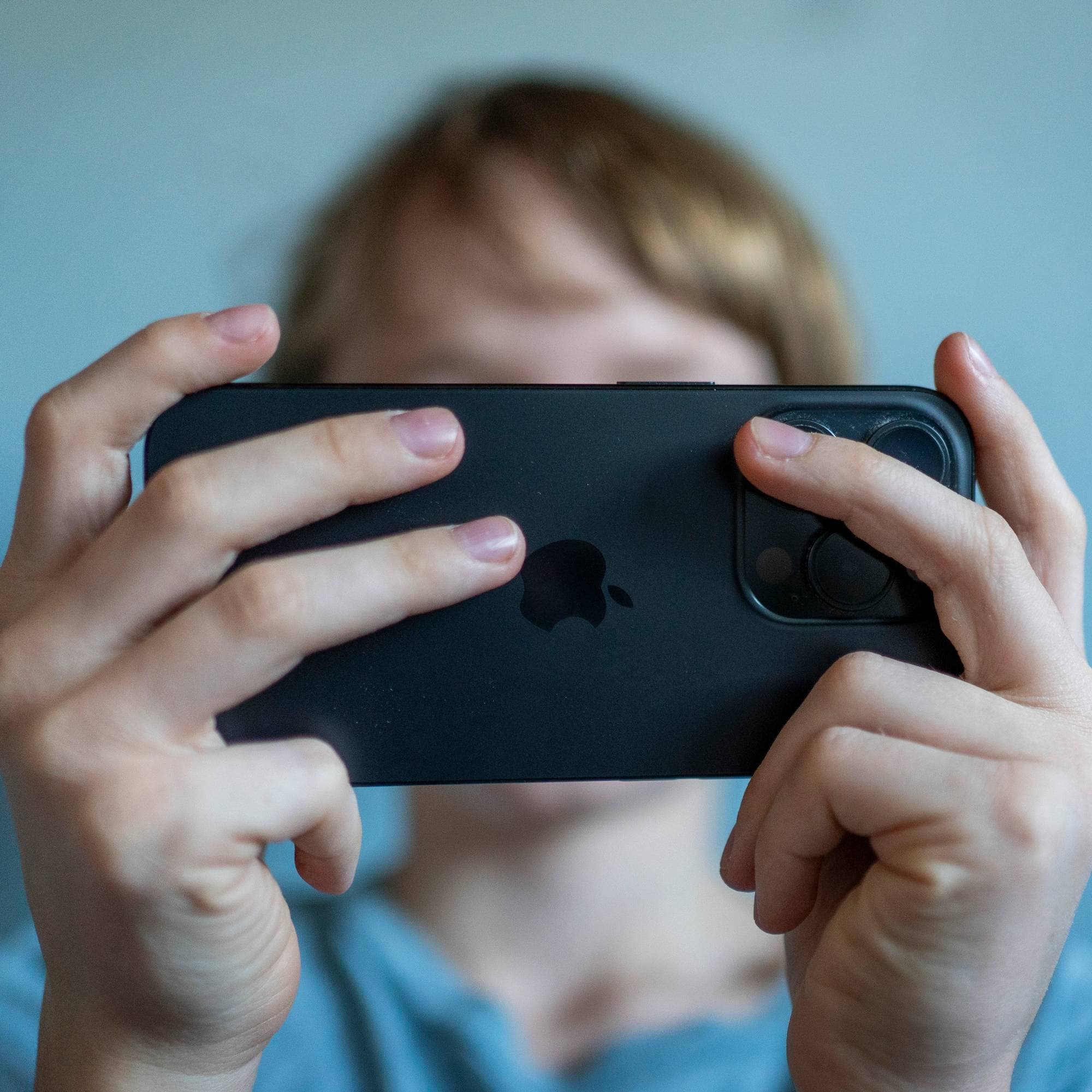 Et bilde av et barn som holder en mobiltelefon. Ansiktet er ikke synlig. 