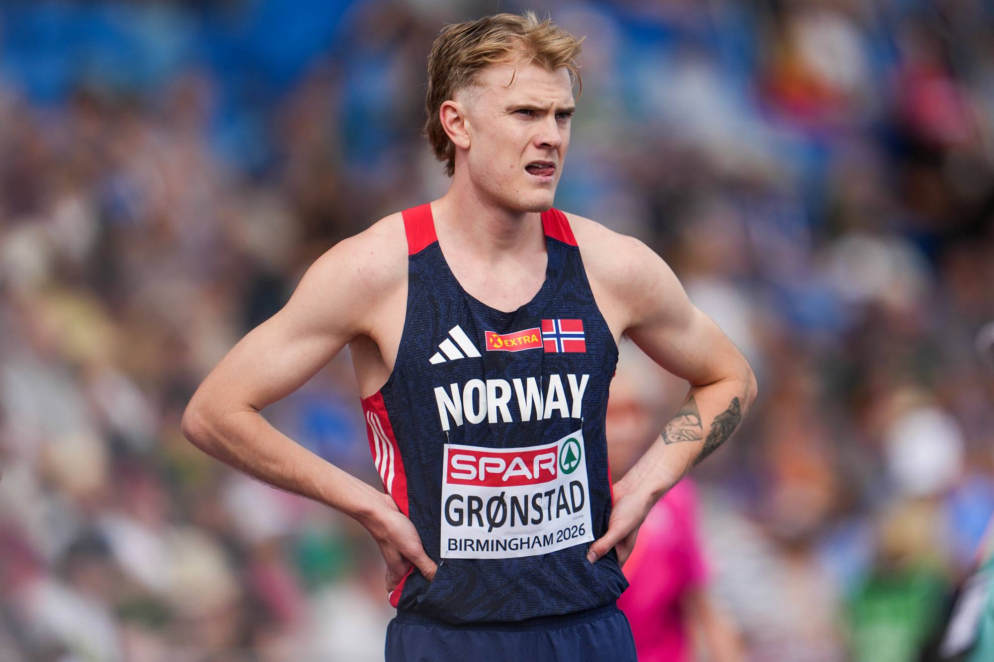 Friidrettsutøver Tobias Grønstad i norsk landslagsdrakt med hendene i siden på en stadion. (Bildebeskrivelsen er laget av en KI-tjeneste)