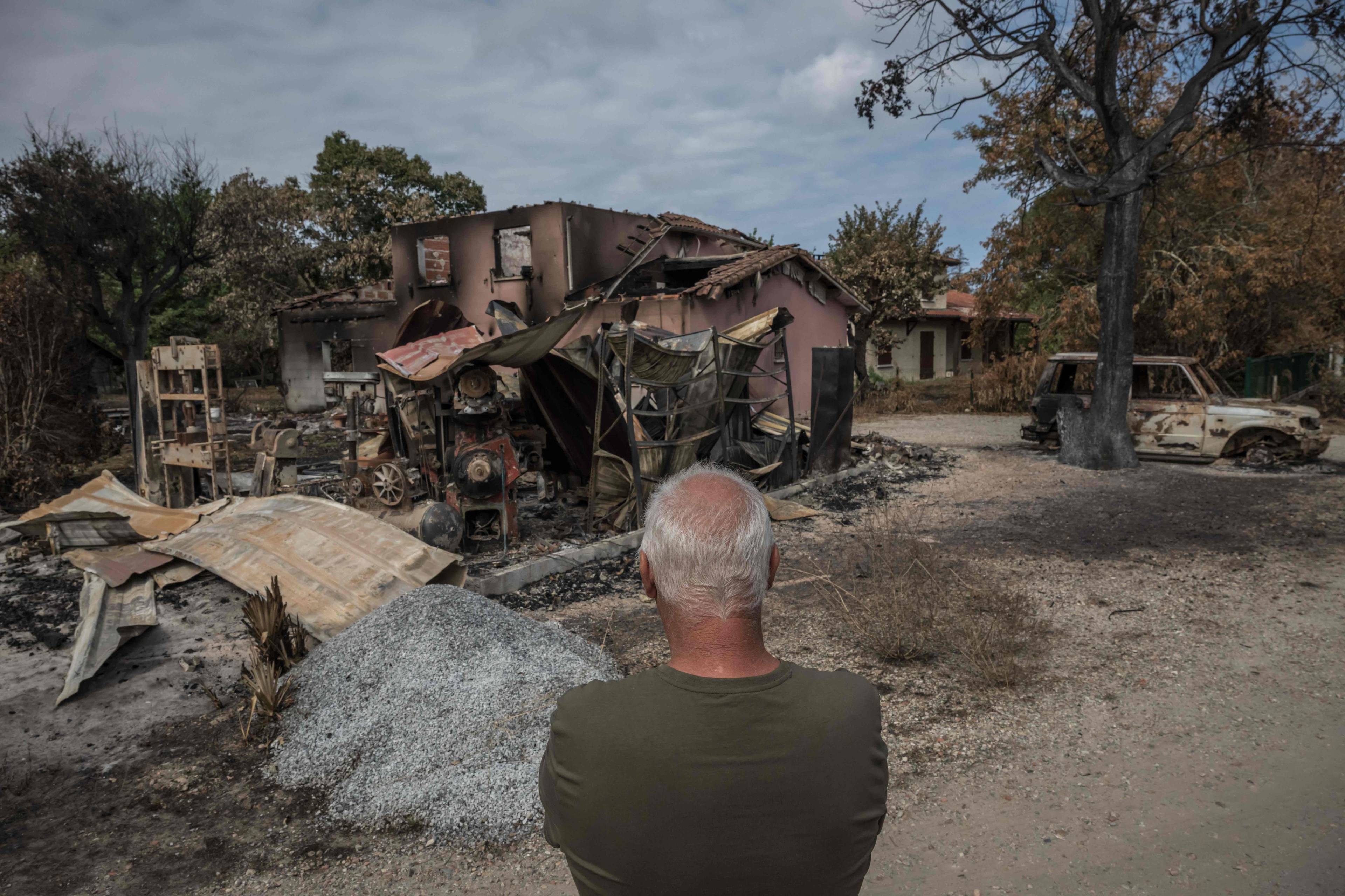 Mann ser på et utbrent hus og vraket bil etter skogbrann. (Bildebeskrivelsen er laget av en KI-tjeneste)