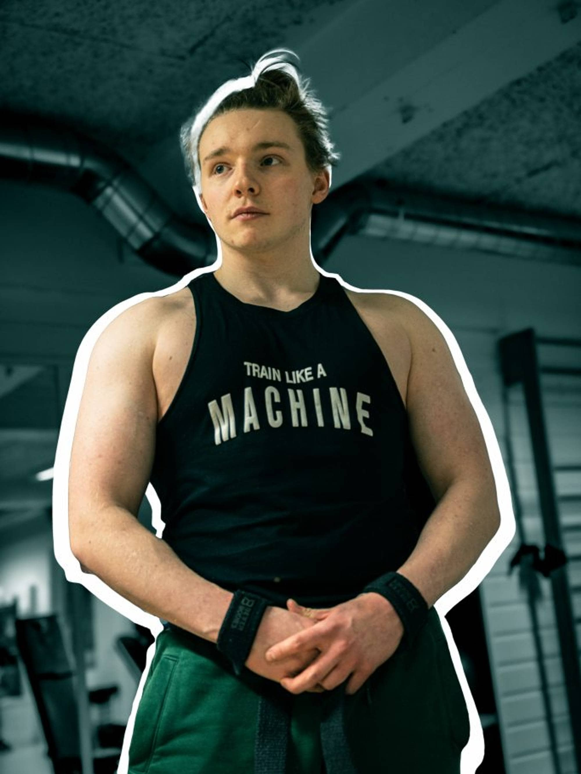 Bilde av Ian som flekser brystkassen og holder hendene samlet. Han har på seg en singlet hvor det står "train like a machine" og grønne joggebukser. Håret er gyllenbrunt og i en dott på hodet. 