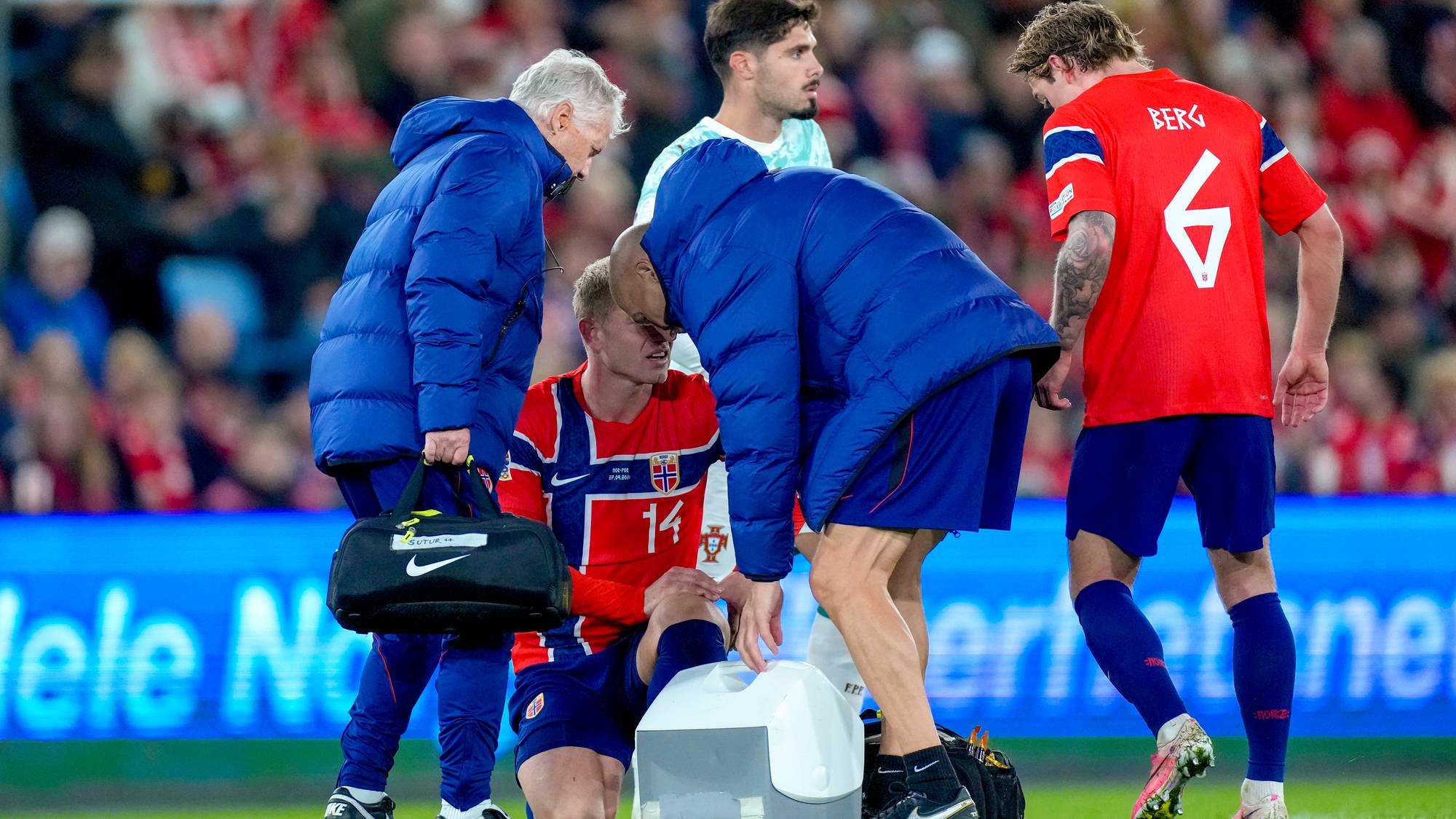 Medisinsk personell hjelper en skadet norsk fotballspiller på banen mens lagkamerater ser på. (Bildebeskrivelsen er laget av en KI-tjeneste)
