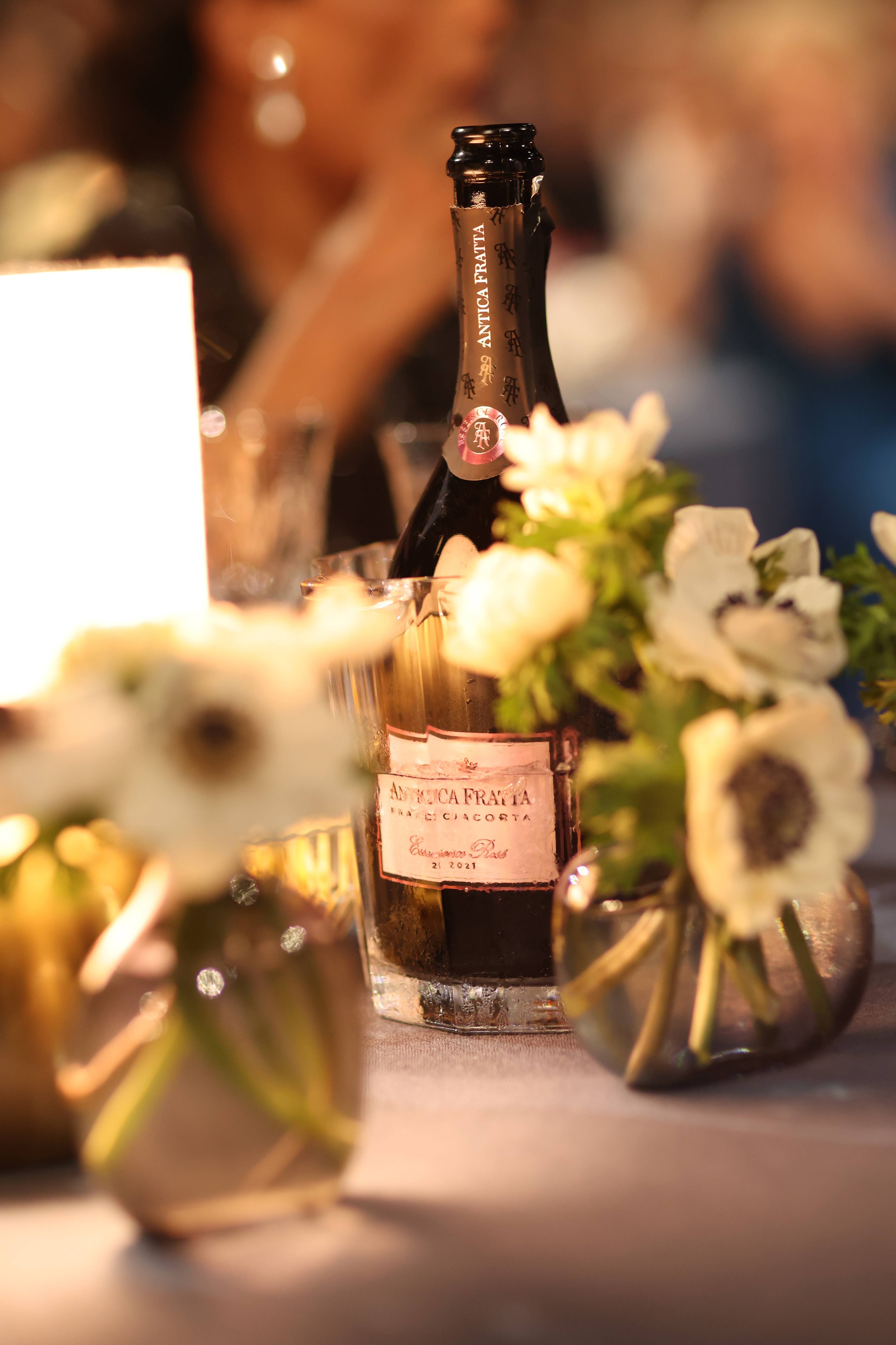 En flaske Antica Fratta musserende vin i en kjøler på et bord dekket med hvite blomster. (Bildebeskrivelsen er laget av en KI-tjeneste)