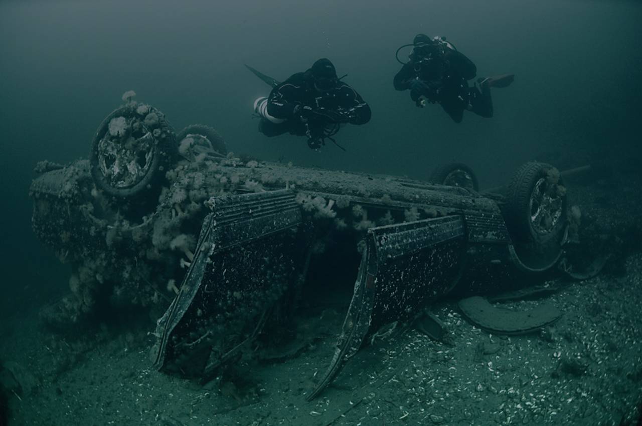 Dykkere ser på en Mercedes liggende opp ned på havbunnen.