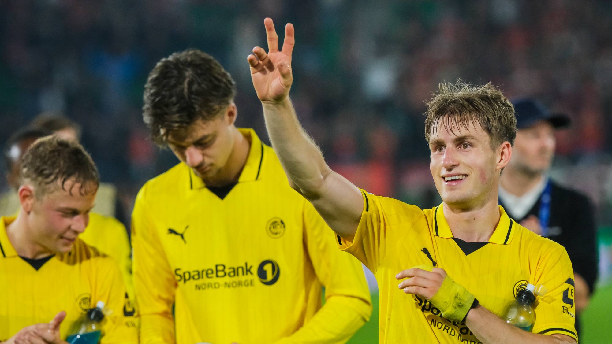 Fotballspiller i gul drakt viser tre fingre med hånden hevet etter en kamp på en stadion. (Bildebeskrivelsen er laget av en KI-tjeneste)