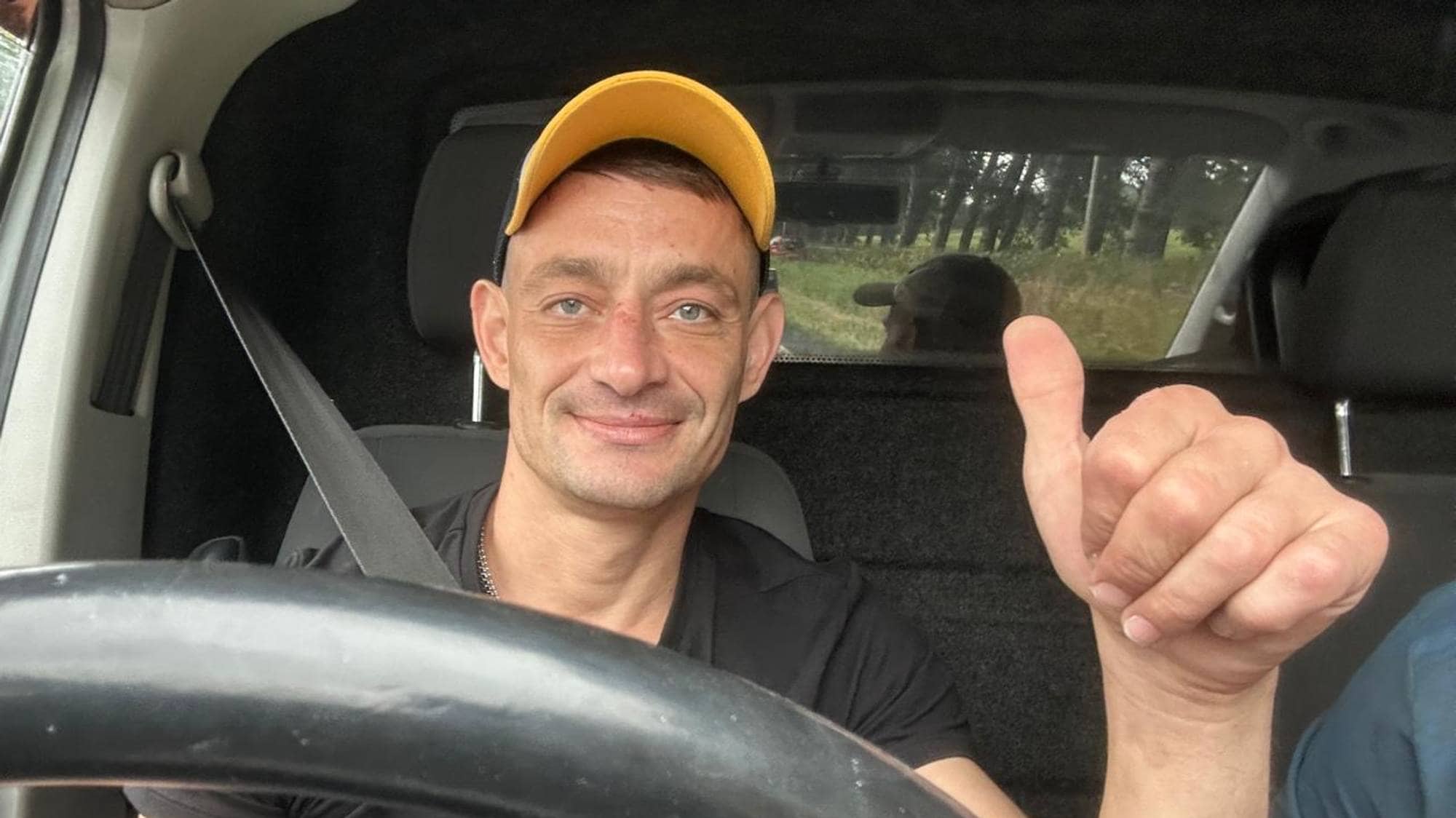 Sergiu Tincaburov smiler og viser tommel opp, han sitter bak rattet i en bil. 