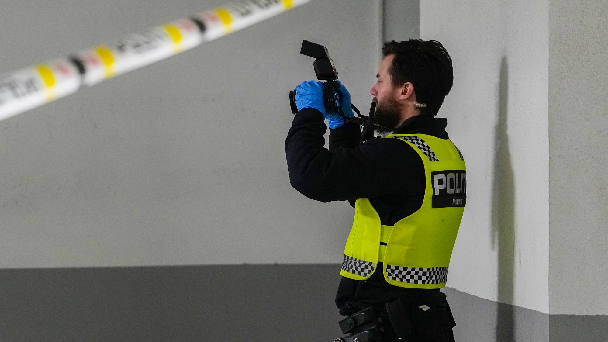 Politiets kriminaltekniker fotograferer et åsted bak sperrebånd. (Bildebeskrivelsen er laget av en KI-tjeneste)