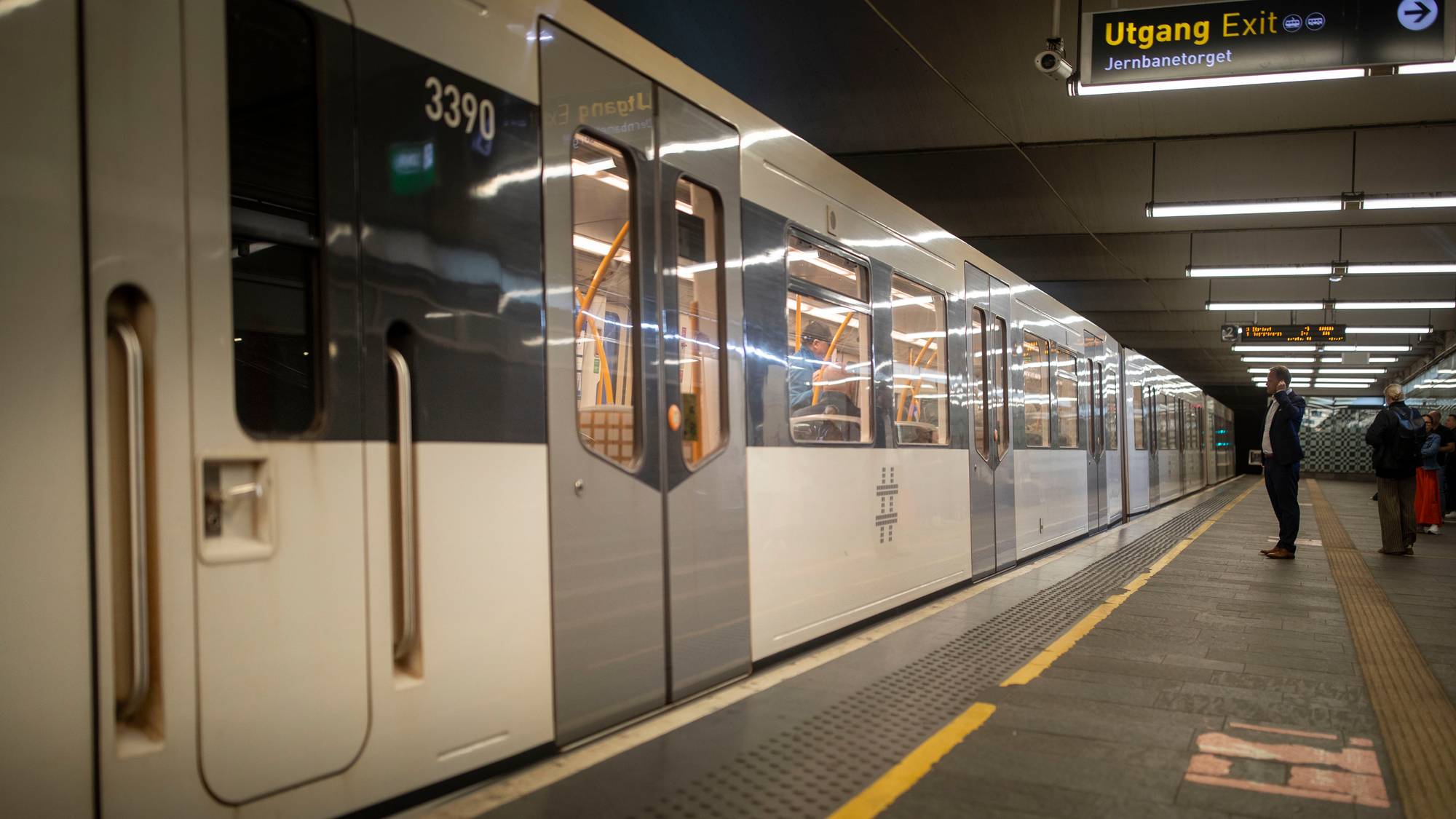 T-banevogn stående på perrong ved Jernbanetorget stasjon. Personer venter på plattformen. (Bildebeskrivelsen er laget av en KI-tjeneste)