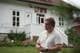 Håvard Greger Hagen / NRK En mann med armene foldet foran seg står utenfor en hvit bygning med røde bokstaver som leser "UTØYA". Mannen har lukket øynene og ser ut til å være i ettertanke. En hage med blomster er synlig i forgrunnen. Bygningen er en hvit trebygning med flere vinduer og en trapp. (Bildebeskrivelsen er laget av en KI-tjeneste)