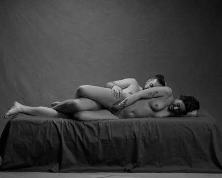 En naken dame ligger på siden i senga med en naken mann liggende bak seg.