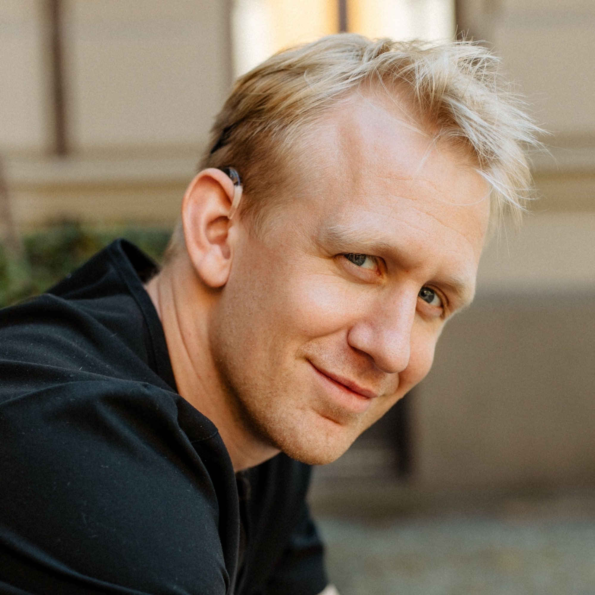 Portrett av en lyshåret mann i sort T-skjorte, med et synlig høreapparat.