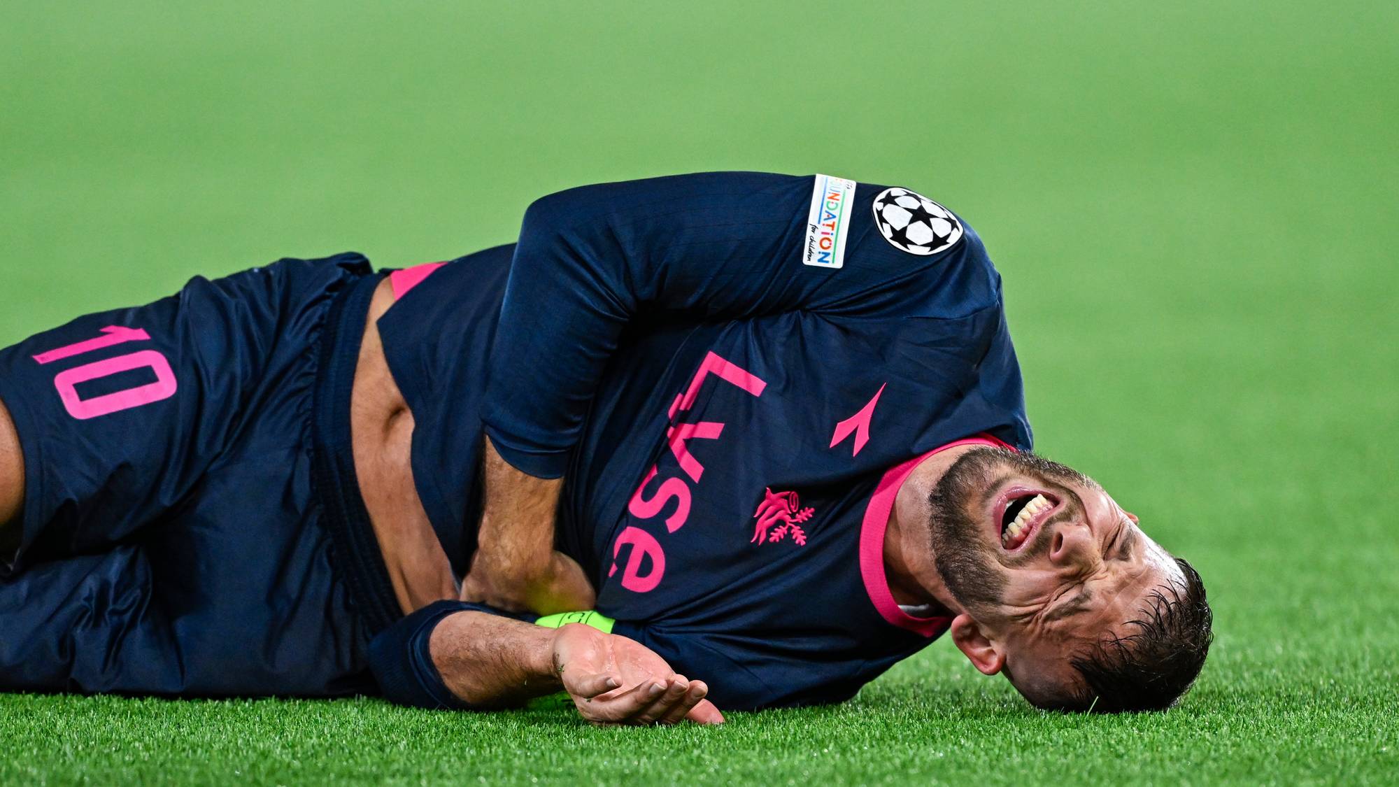 Fotballspiller i Viking-drakt ligger på gresset og holder seg til magen med et tydelig smerteuttrykk. (Bildebeskrivelsen er laget av en KI-tjeneste)