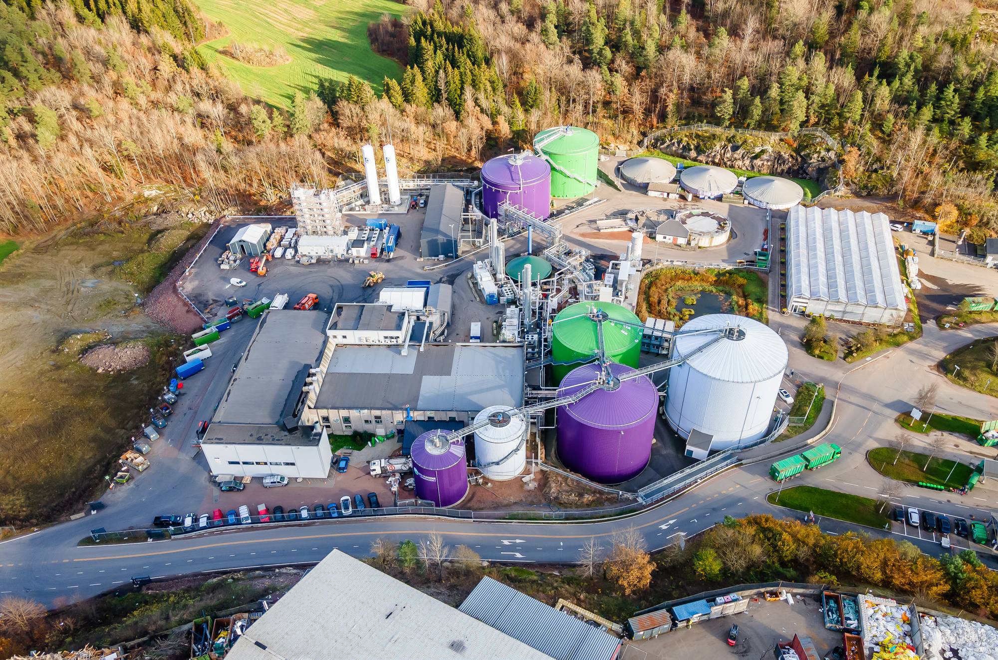 Industrianlegg med fargerike tanker innimellom skog og jorder. 