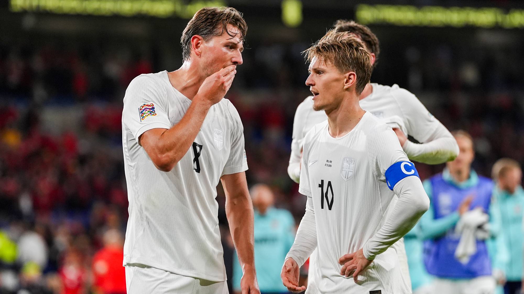 Morten Thorsby og Martin Ødegaard i hvite landslagsdrakter snakker sammen på fotballbanen. (Bildebeskrivelsen er laget av en KI-tjeneste)