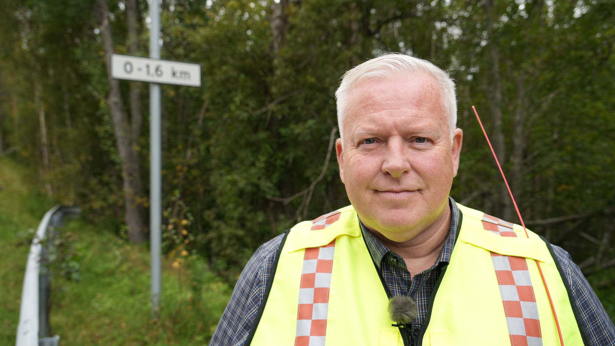 Tor Eriksen, nestleder i Målselv viltnemnd ser inn i kamera. Har på seg refleksvest. I bakgrunnen ser vi et skilt med 0-1.6 km, og det er tydelig at det mangler et skilt over det. 