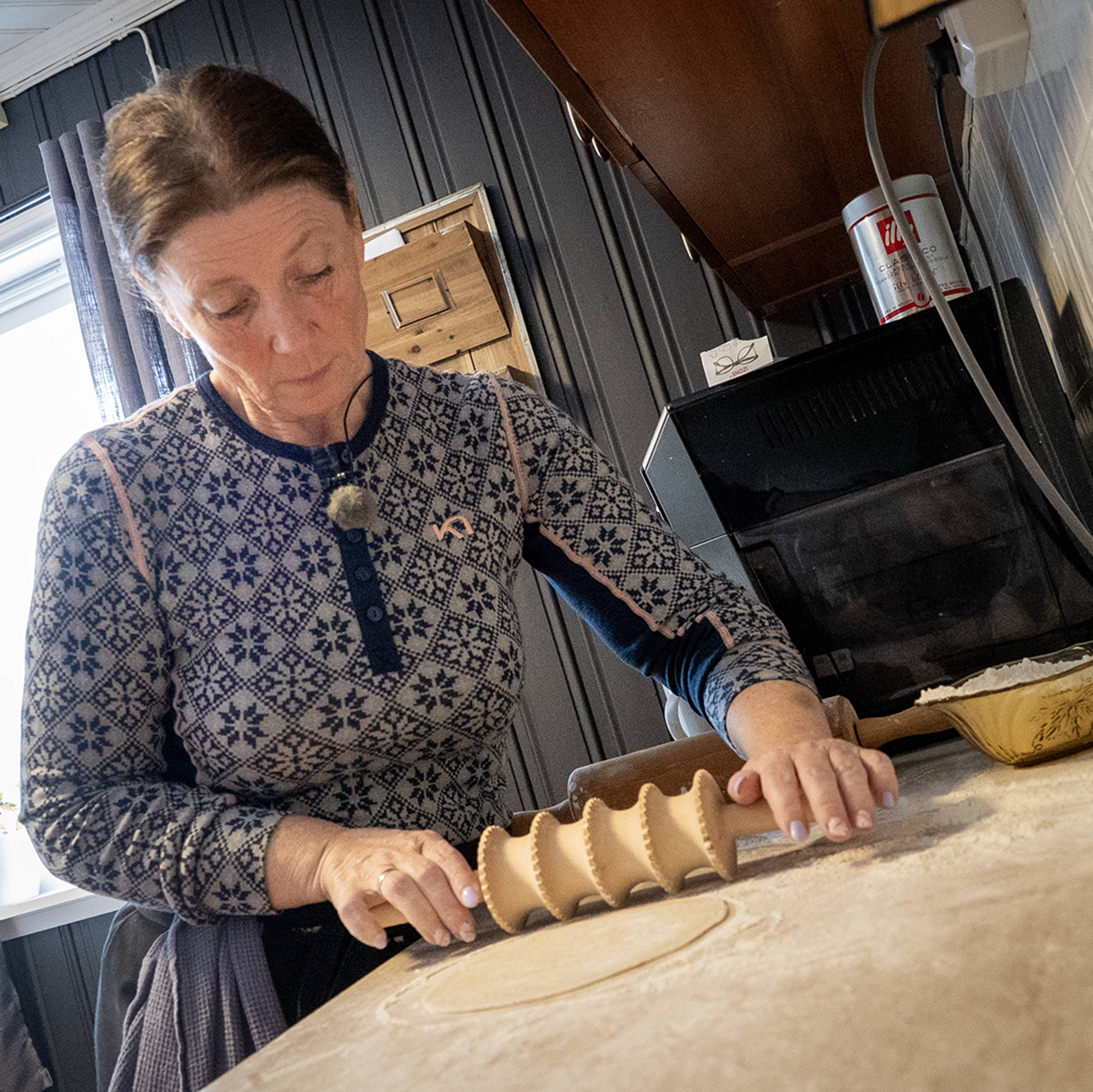 Kvinne med mørkt hår i blå ullgenser med spesiell kjevle og bakst på kjøkkenbenken.