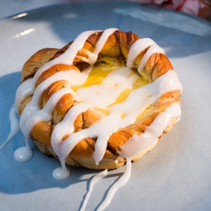 En solskinnsbolle, altså en kanelsnurr med gul krem og melisglasur ligger på et fat.