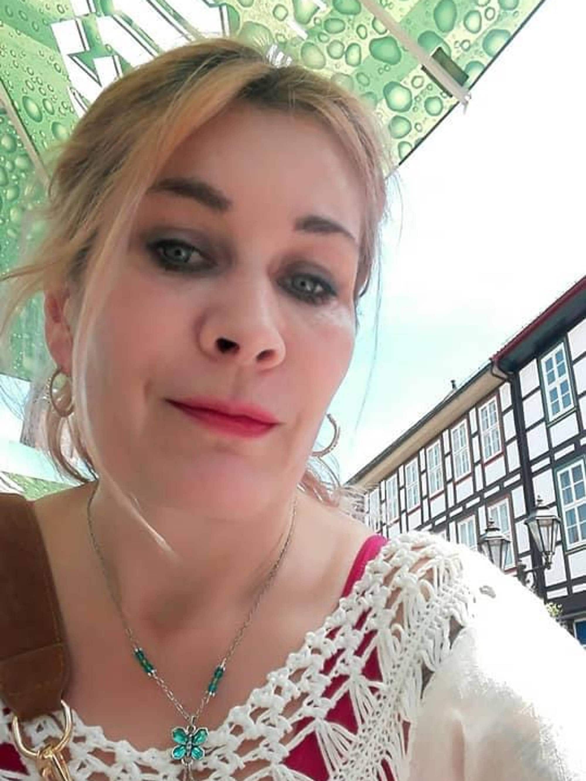 Kvinne med lyst hår tar en selfi utendørs foran en bygning. (Bildebeskrivelsen er laget av en KI-tjeneste)