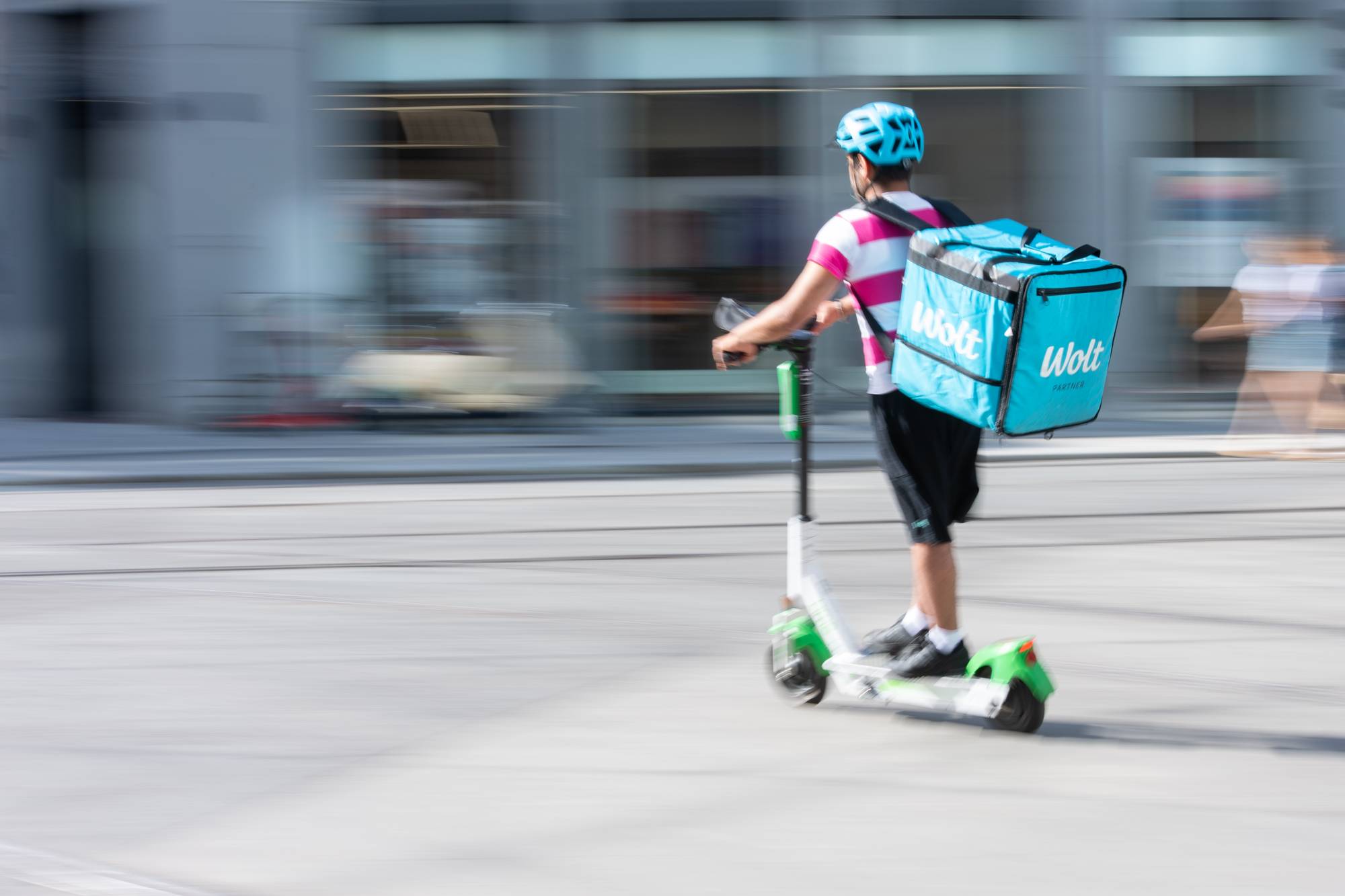en ung mann som kjører scooter med en Wolt-bag på ryggen