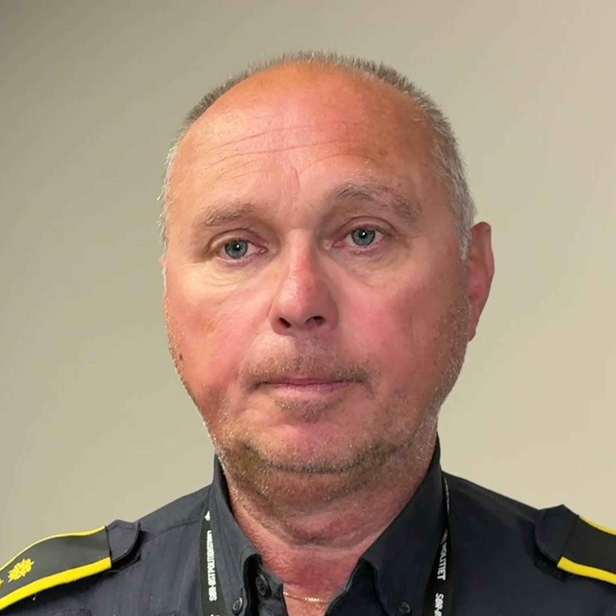 En mann står i en sort politiuniform og ser rett i kamera. Han har et nøytralt uttykk i fjeset.