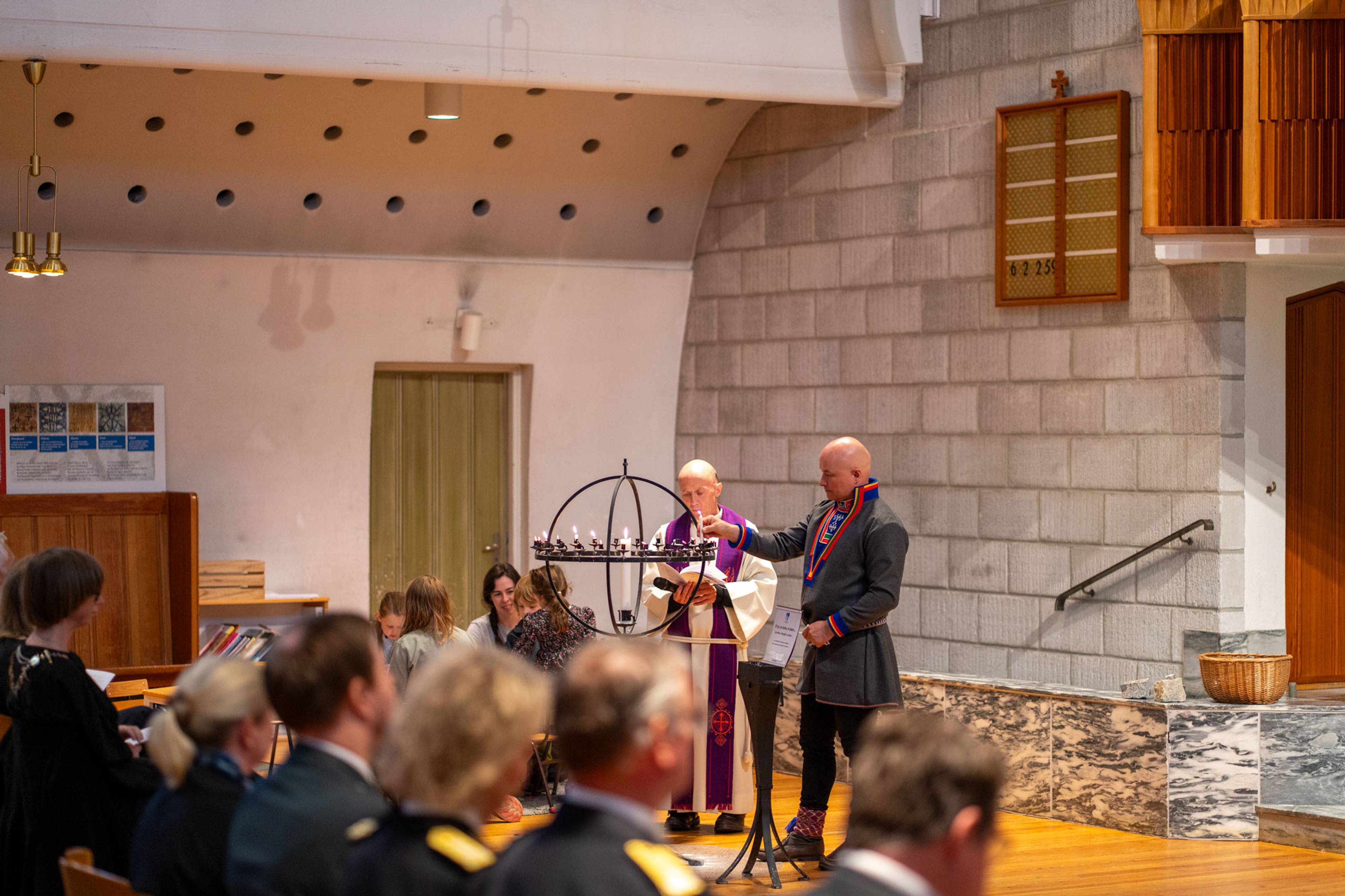 Mennesker i en kirke, en mann i kofte som tenner på et lys
